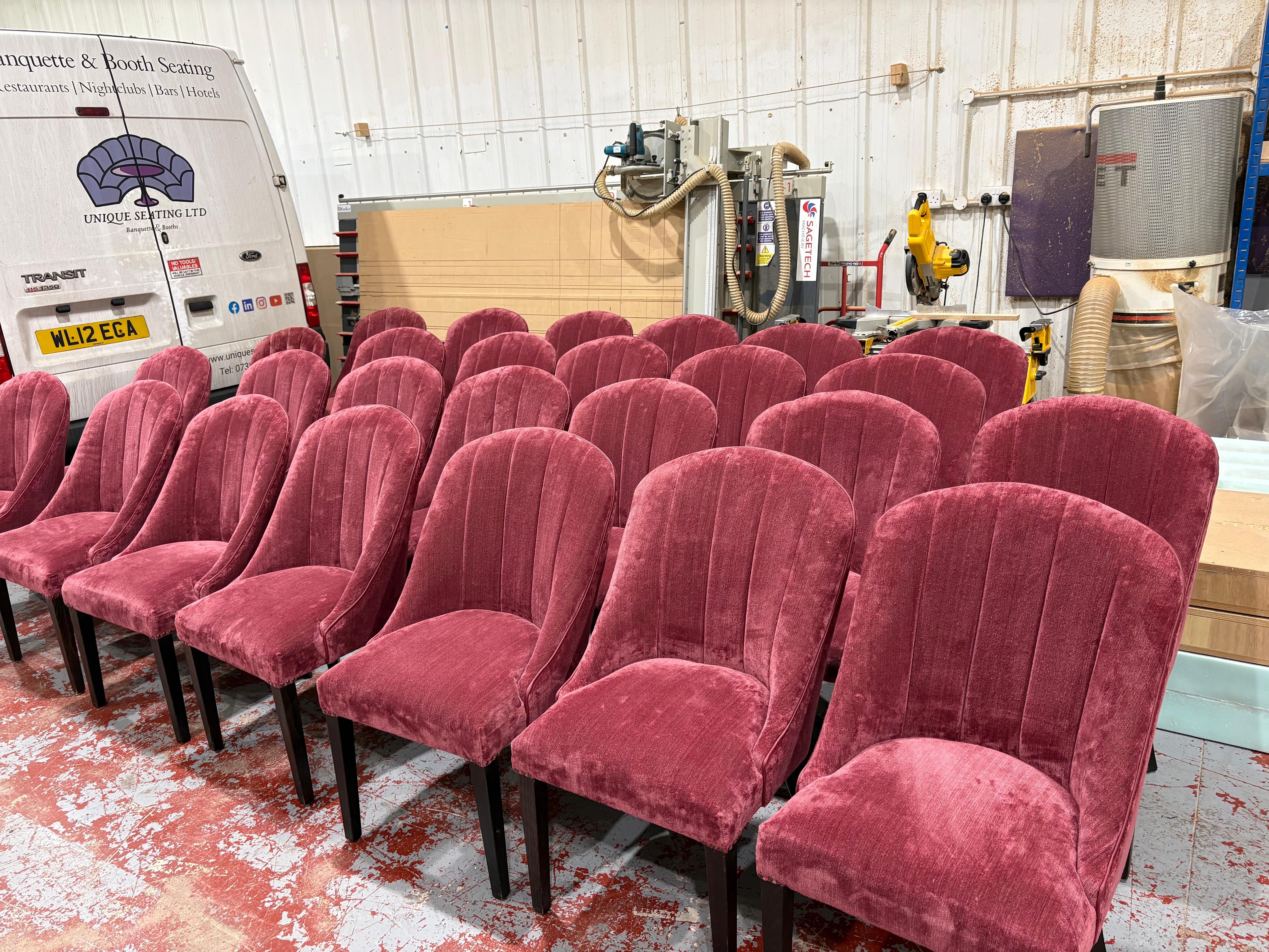 A full set of dining chairs reupholstered in berry red chenille with fluted backs and dark stained legs, lined up in the workshop.