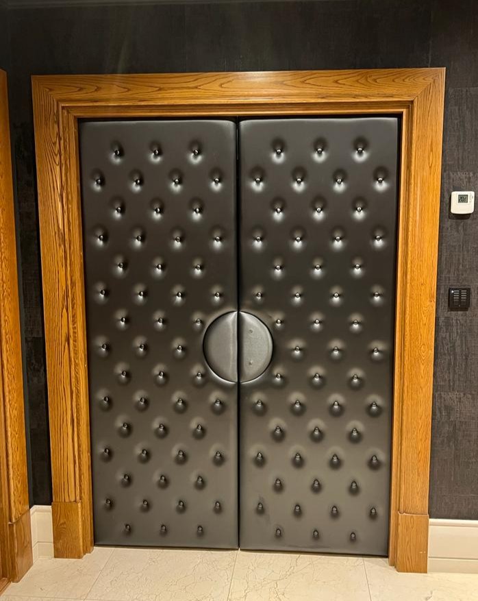 Double doors faced in black leather with deep buttoning and a padded circular pull, set into an oak frame.