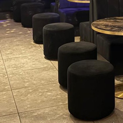 Low round stools in black velvet, made to tuck under marble-topped tables in a club lounge.