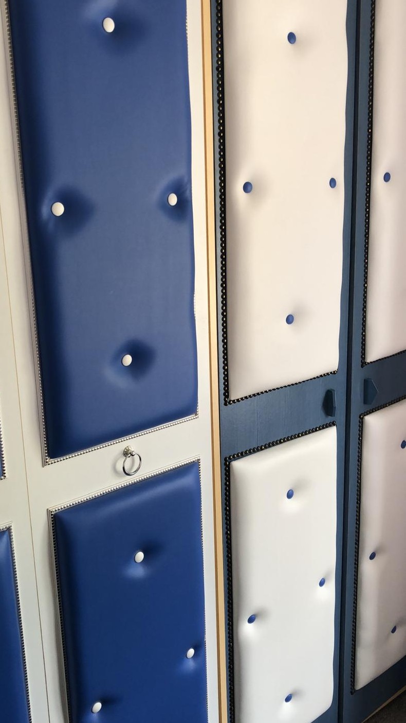 Buttoned leather wall panels in royal blue and cream with contrast buttons and studded borders, framed into painted joinery.
