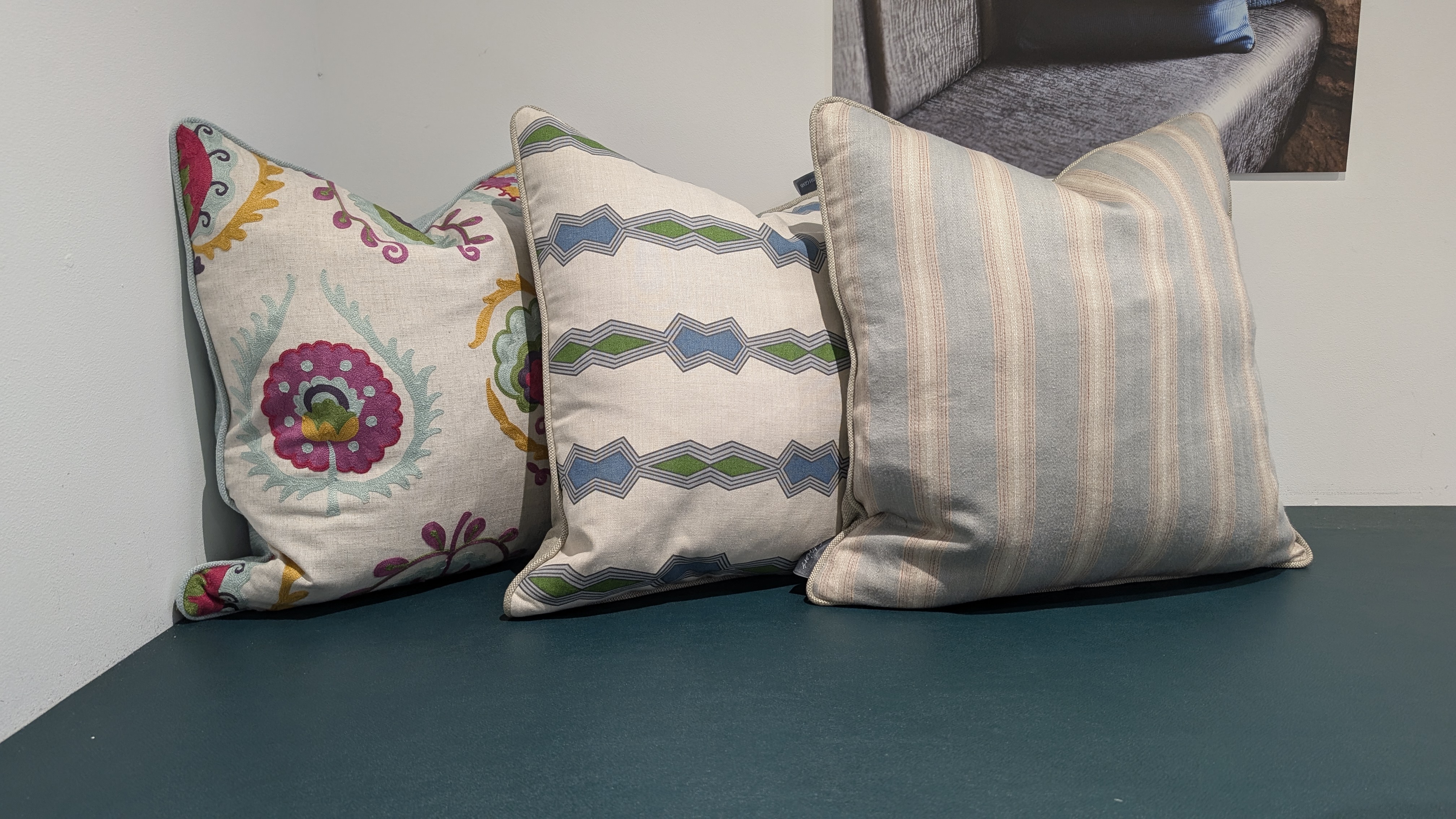 Three piped scatter cushions in embroidered suzani, geometric and soft stripe fabrics on a natural linen ground.