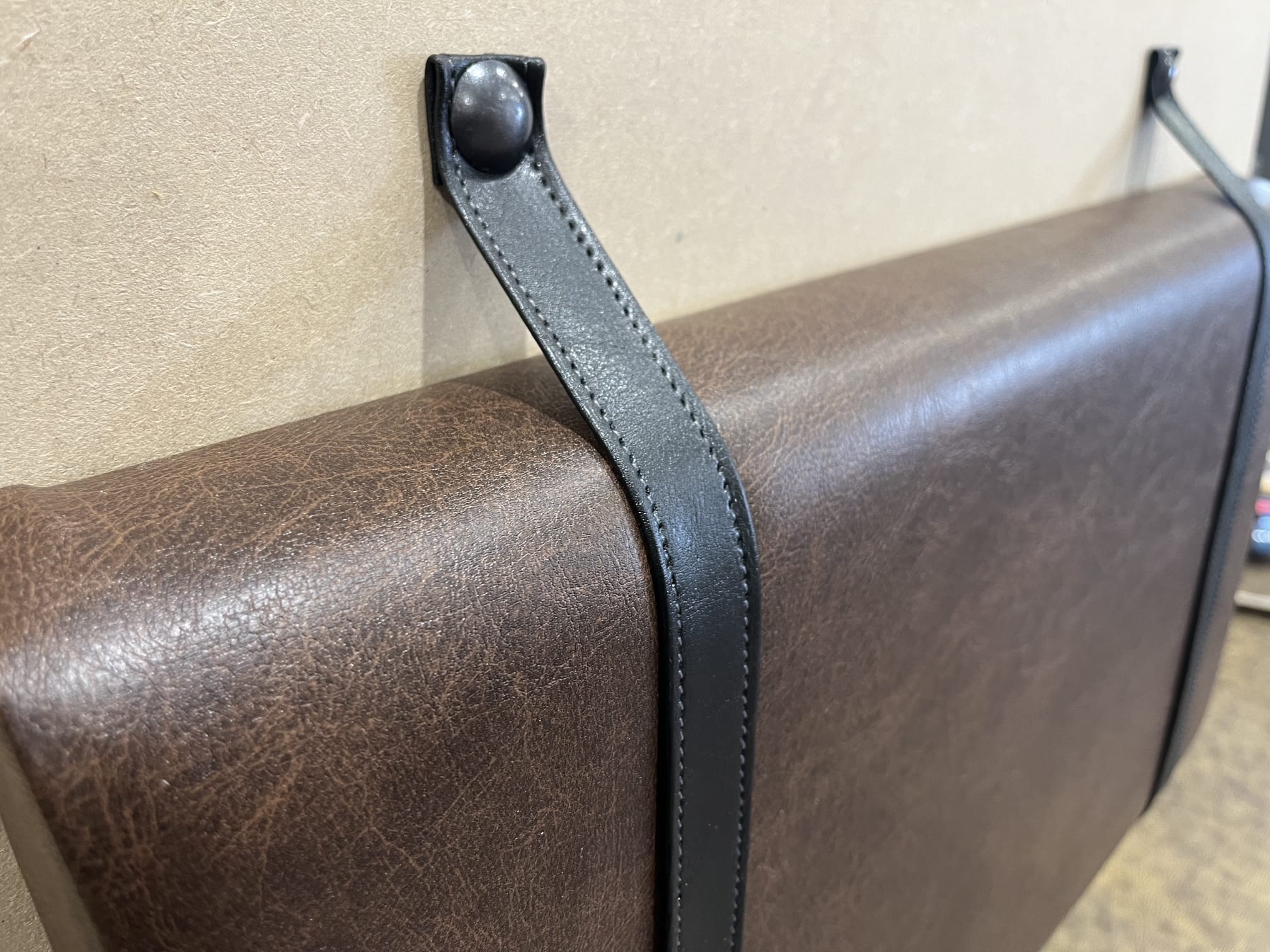 Dark brown faux leather back cushions hung from black leather straps and studs, keeping the wall clear behind a banquette.