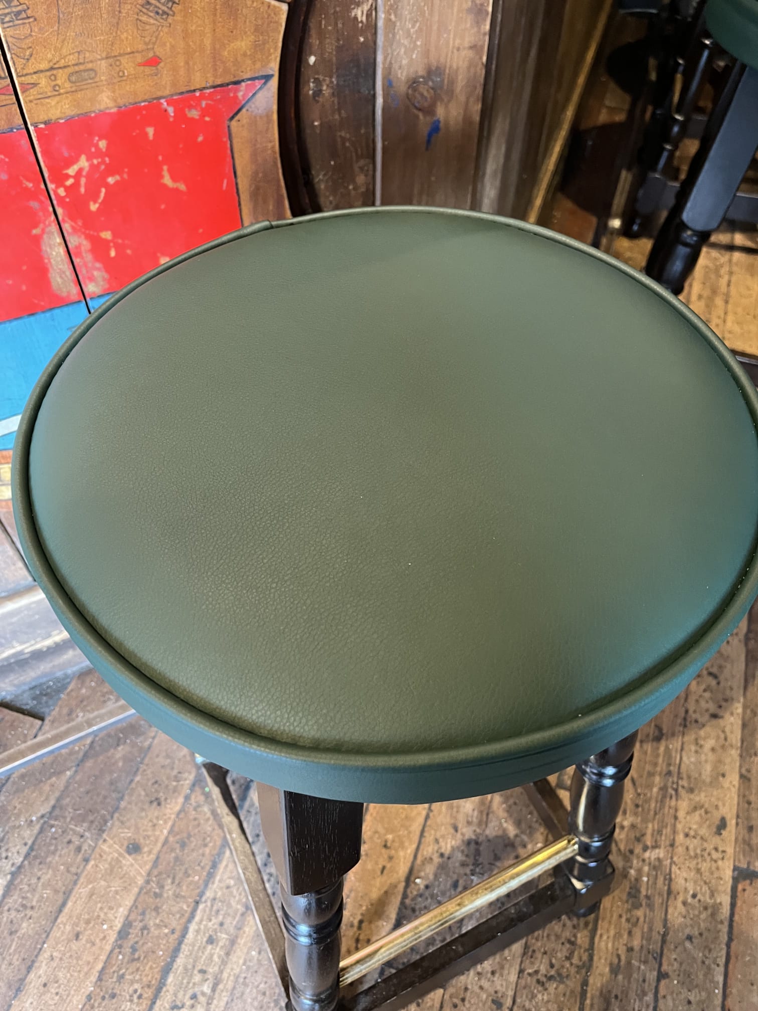 Round stool tops re-covered in forest green leather with a neat piped edge, fitted to black turned pub frames.