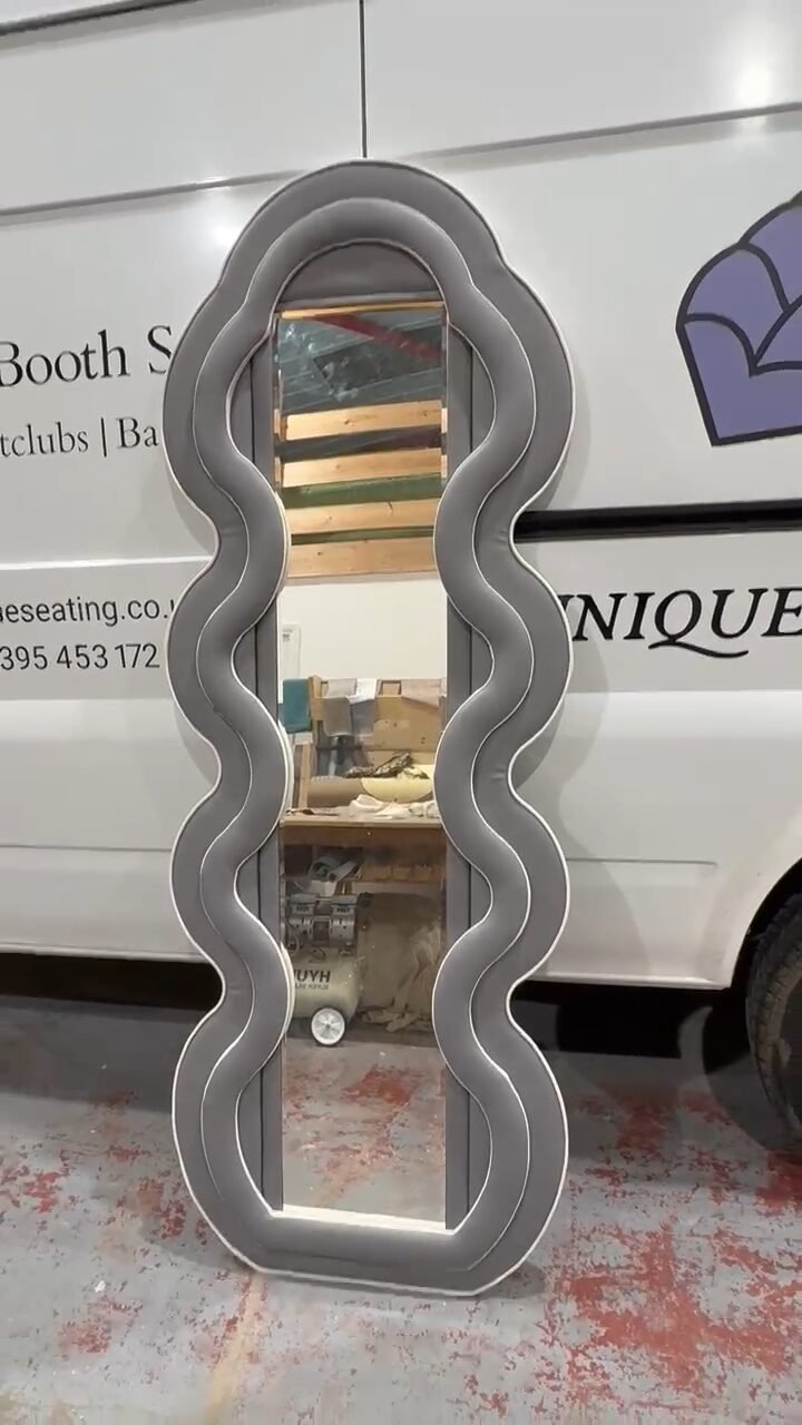 Full-length mirror in a scalloped wave frame upholstered in grey suede, finished at the workshop.