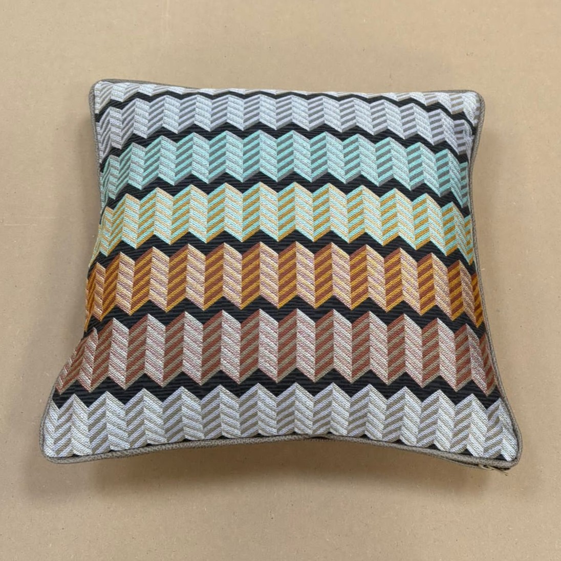 Scatter cushion in a woven zigzag weave running through mint, ochre and rust stripes, with a grey piped edge.