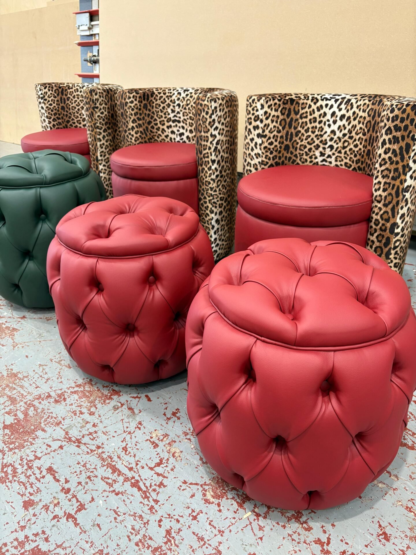 Deep-buttoned red leather drum stools alongside green and leopard-print pieces, finished in the workshop.