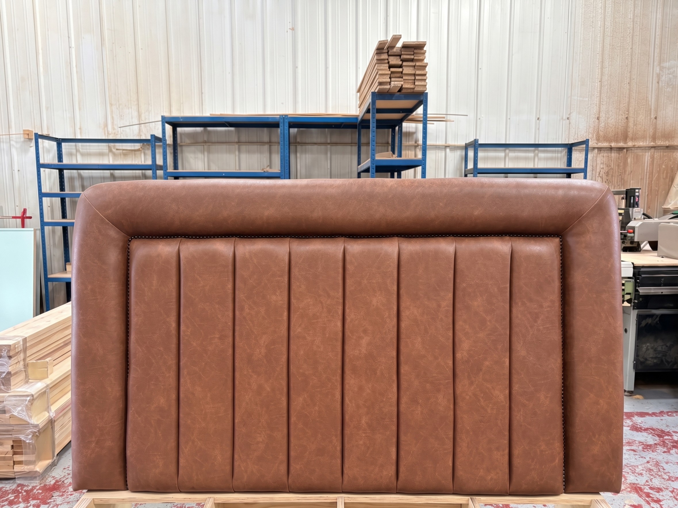 Wide headboard in tan leather with a fluted centre panel, rolled surround and a fine stud border, finished in the workshop.