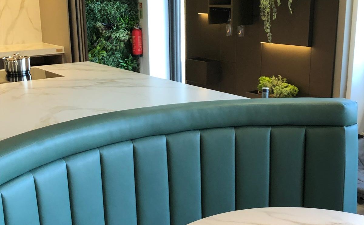 Curved teal leather banquette back with fluted panels and a rolled headrest capping, wrapping a marble island.