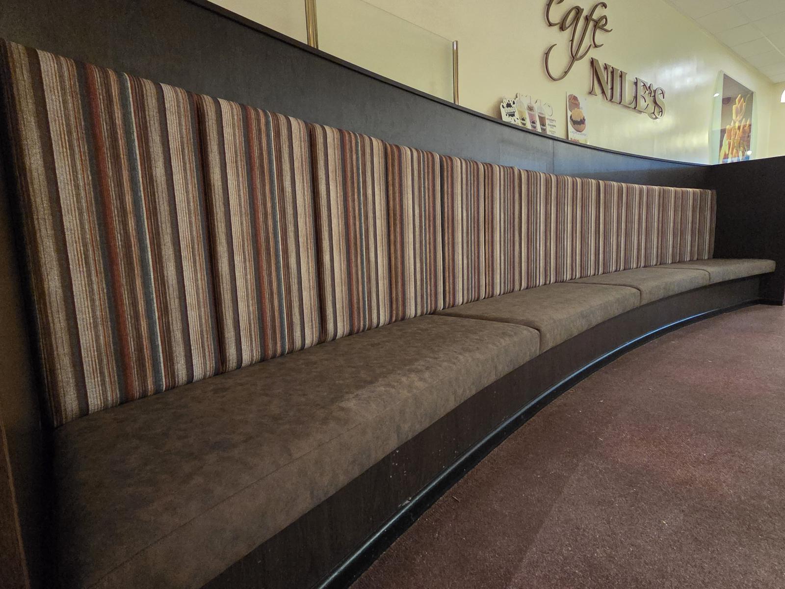 Long curved wall banquette with multi-tone striped panel backrests and a soft brown suede seat, built to follow the sweep of a busy cafe wall.