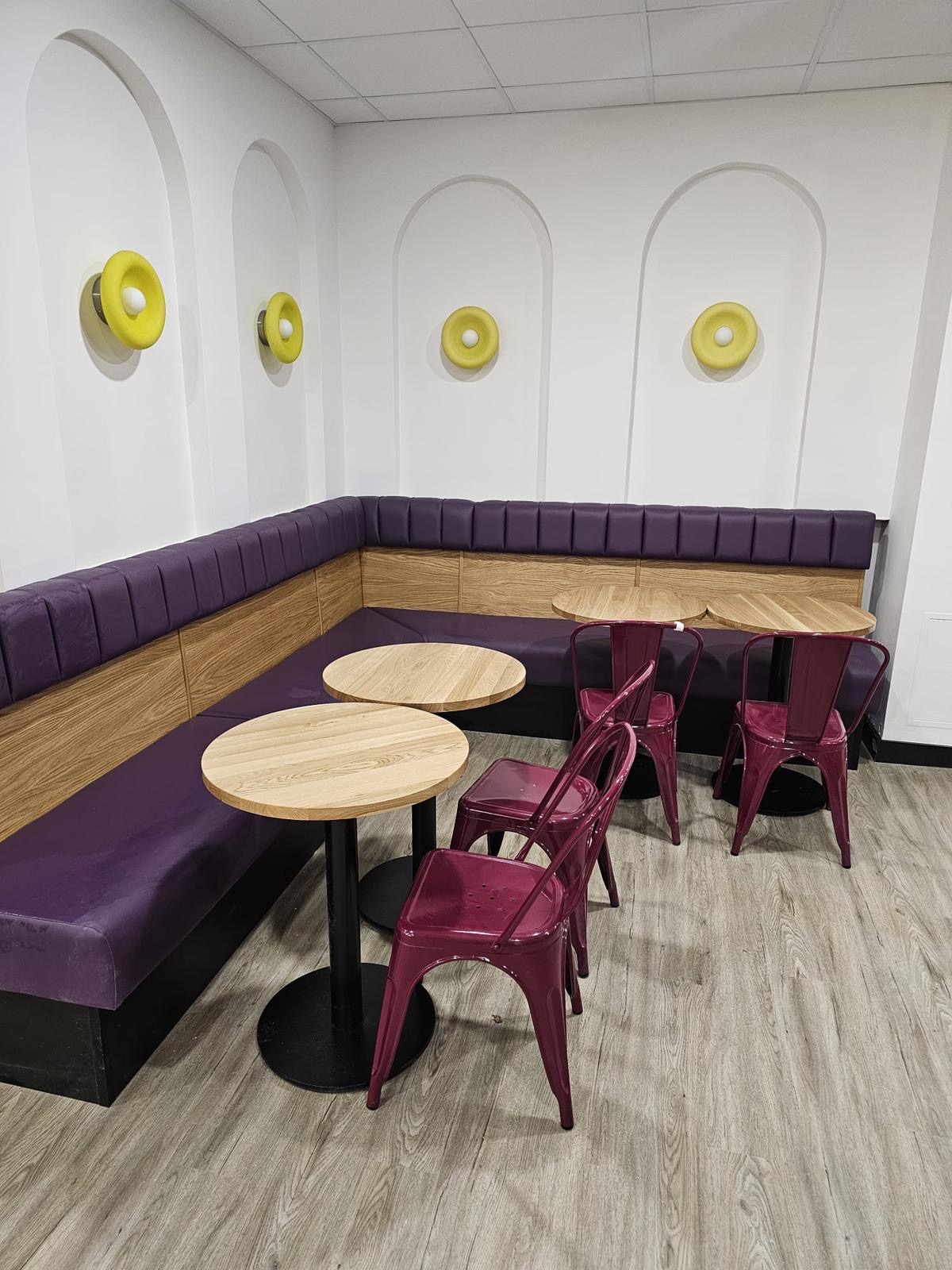 Space-saving purple bench seating with vertical stitch lines, paired with wooden elements and round café tables.