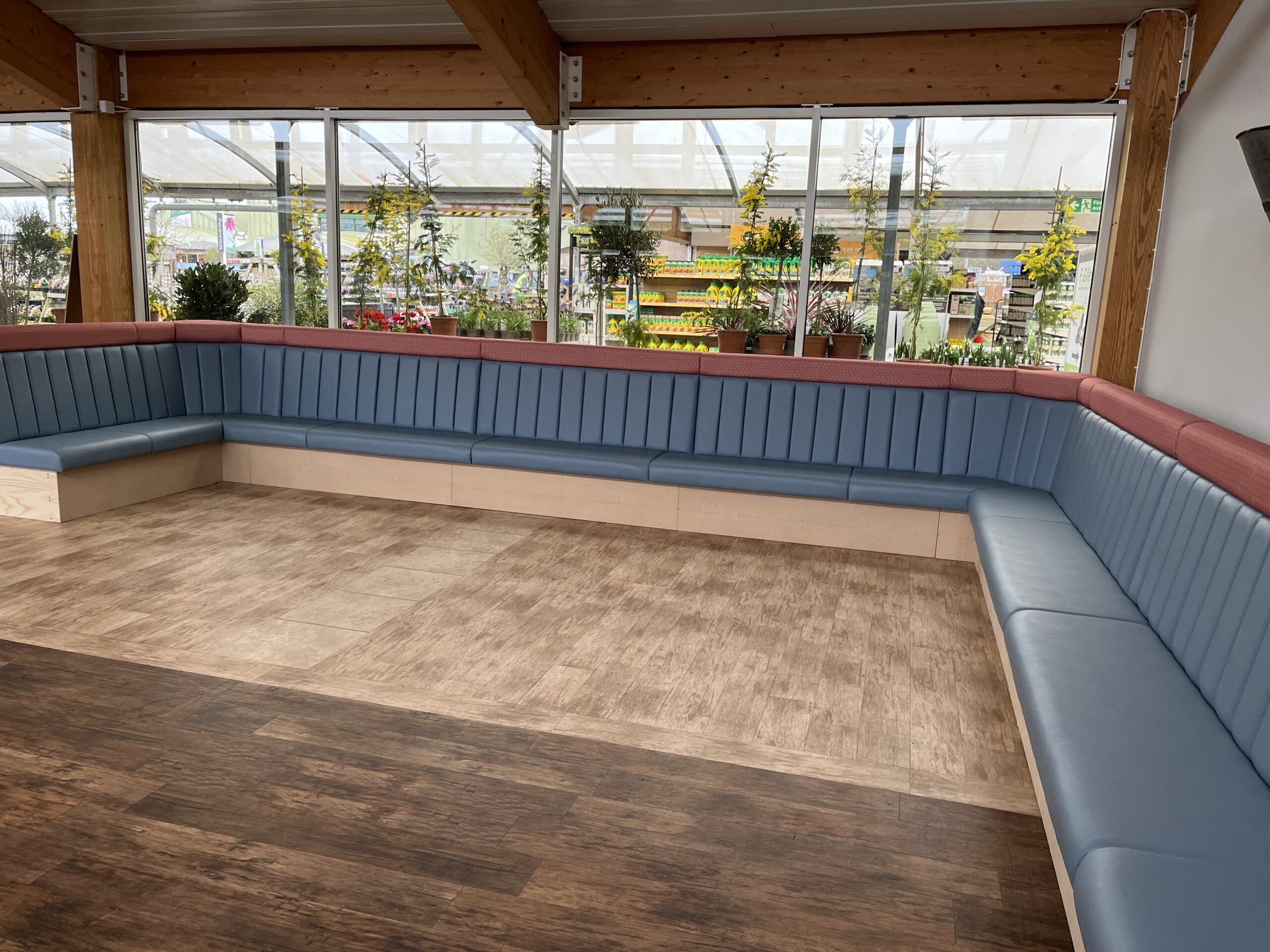 U-shaped fluted banquette in blue leather topped with a red fabric capping rail, built to seat a large garden-centre dining room.