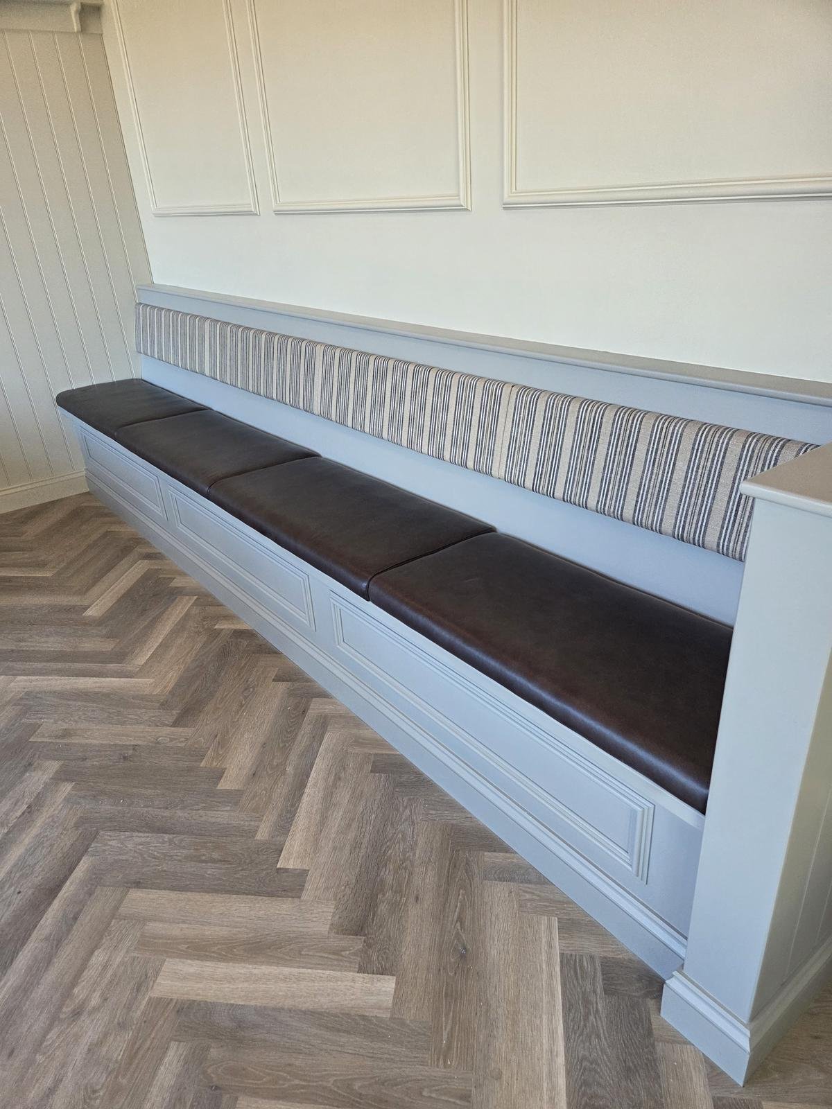 Long wall bench with a dark brown leather seat and slim striped backrest, set into pale blue panelled joinery.