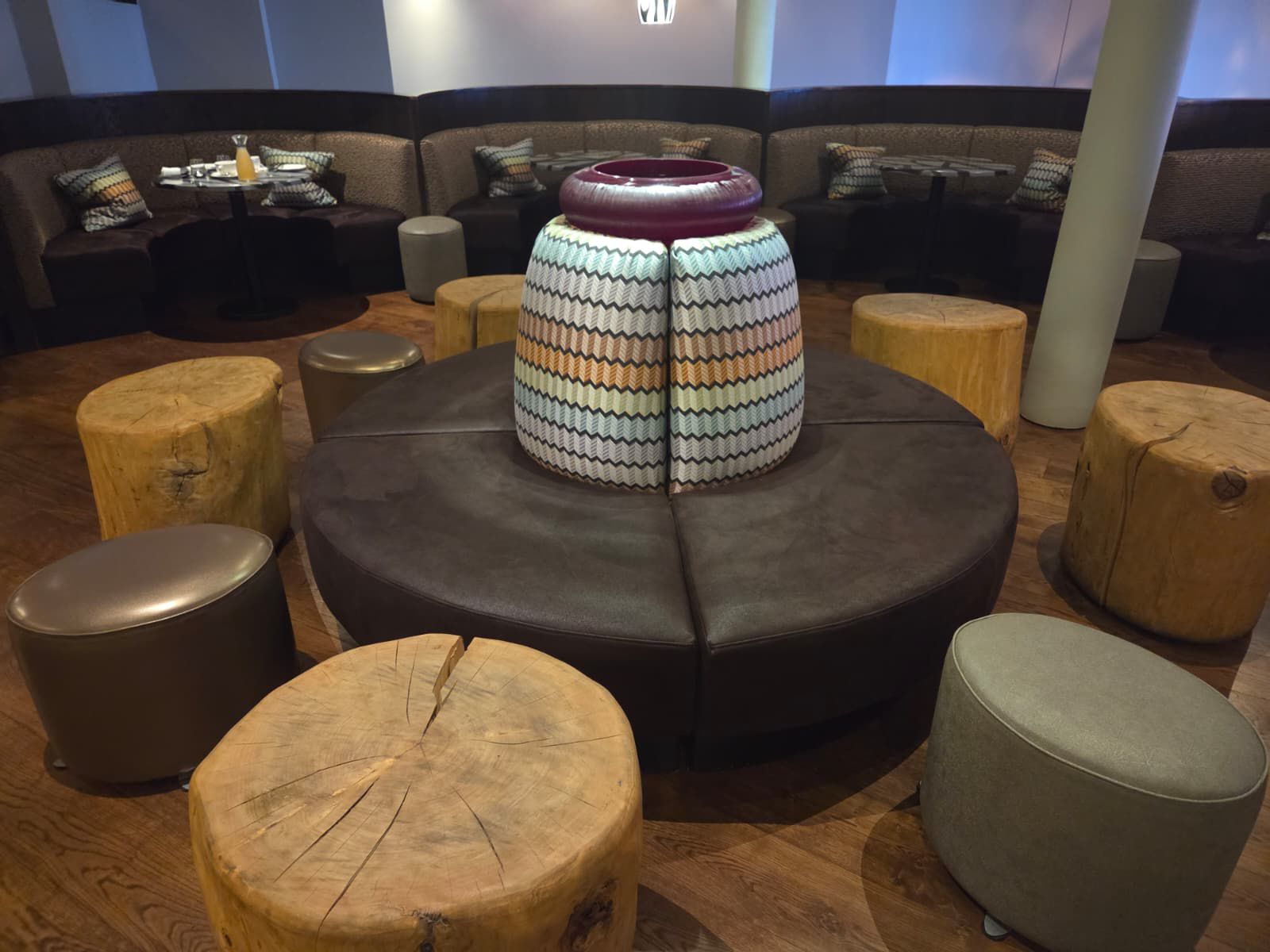 Circular brown leather ottoman built around a zigzag-patterned column, ringed by metallic stools in a hotel lounge.