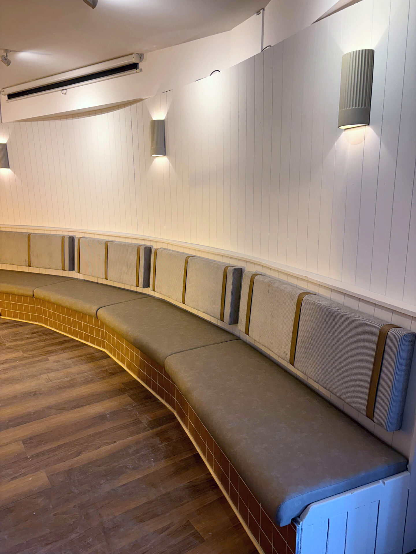 Curved banquette with a stone faux leather seat and individual fabric back panels split by corduroy bolsters.