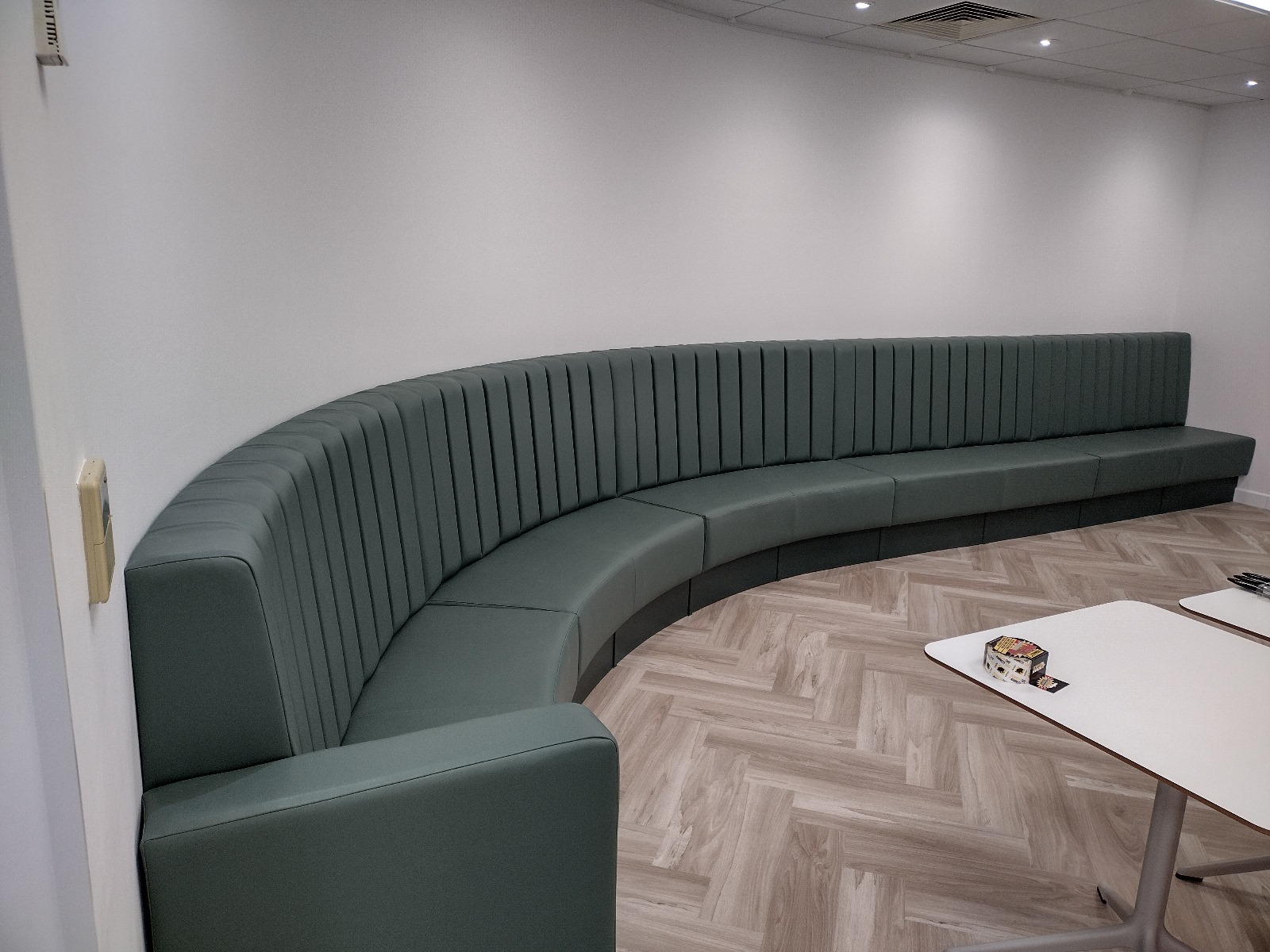 Sweeping fluted bench in sage green faux leather, built to follow the curve of an office breakout area.