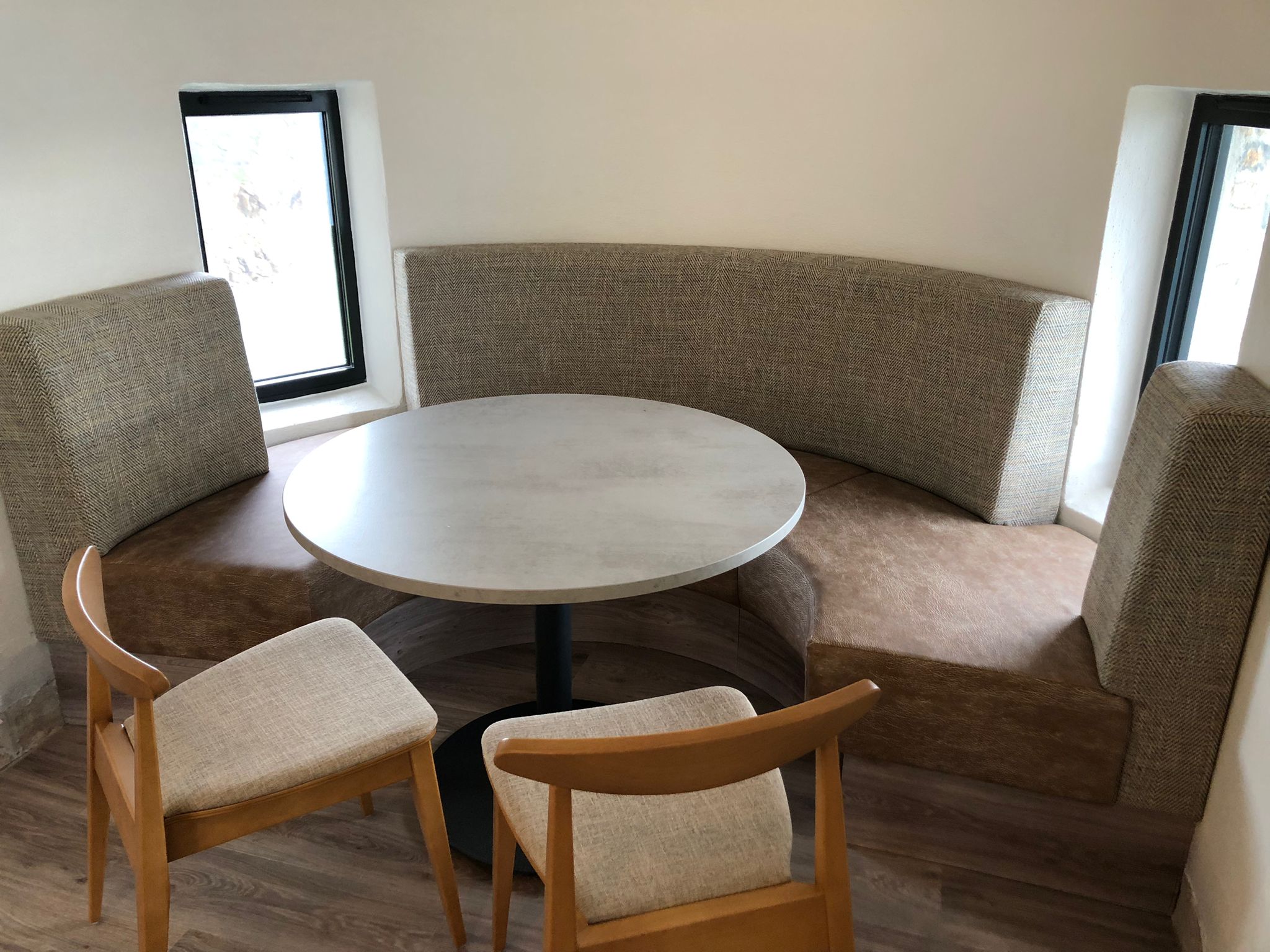 Curved banquette with herringbone tweed backs and a distressed brown leather seat, tucked into a stone window recess.
