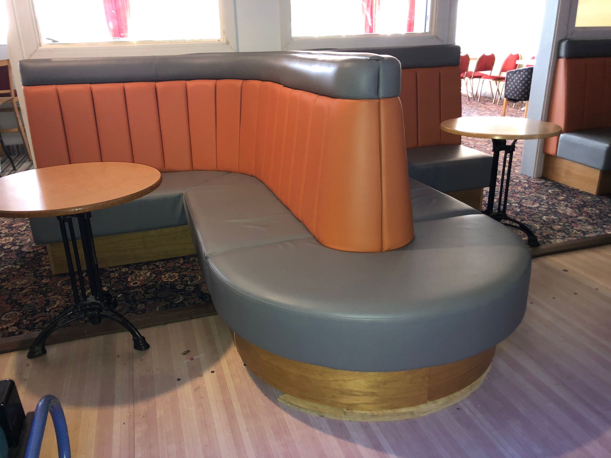 Free-standing serpentine booth with a fluted orange back and grey leather seat, set on a curved timber base.