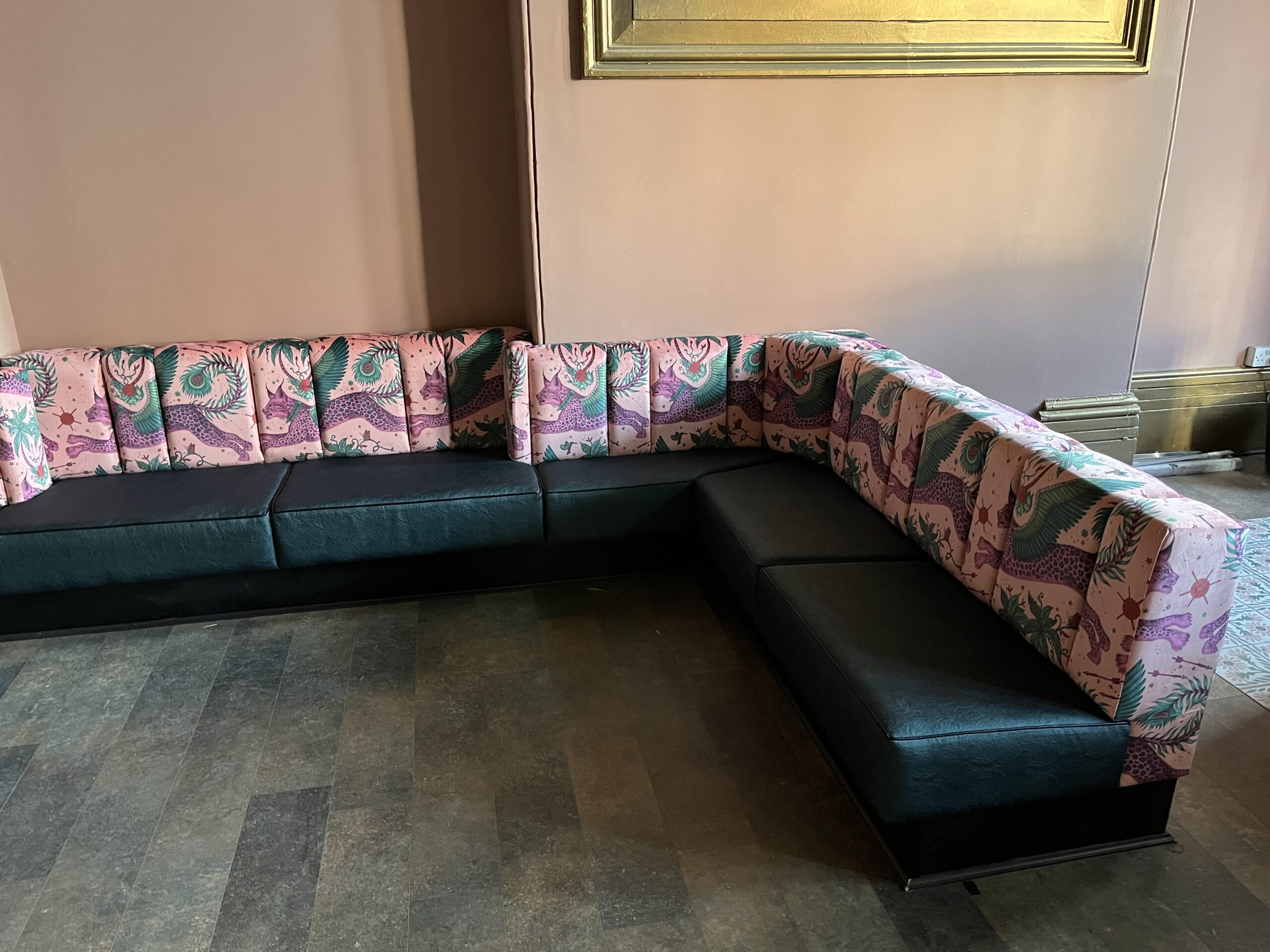 L-shaped banquette with a bold pink animal-print backrest above a black leather seat, built for a bar lounge.