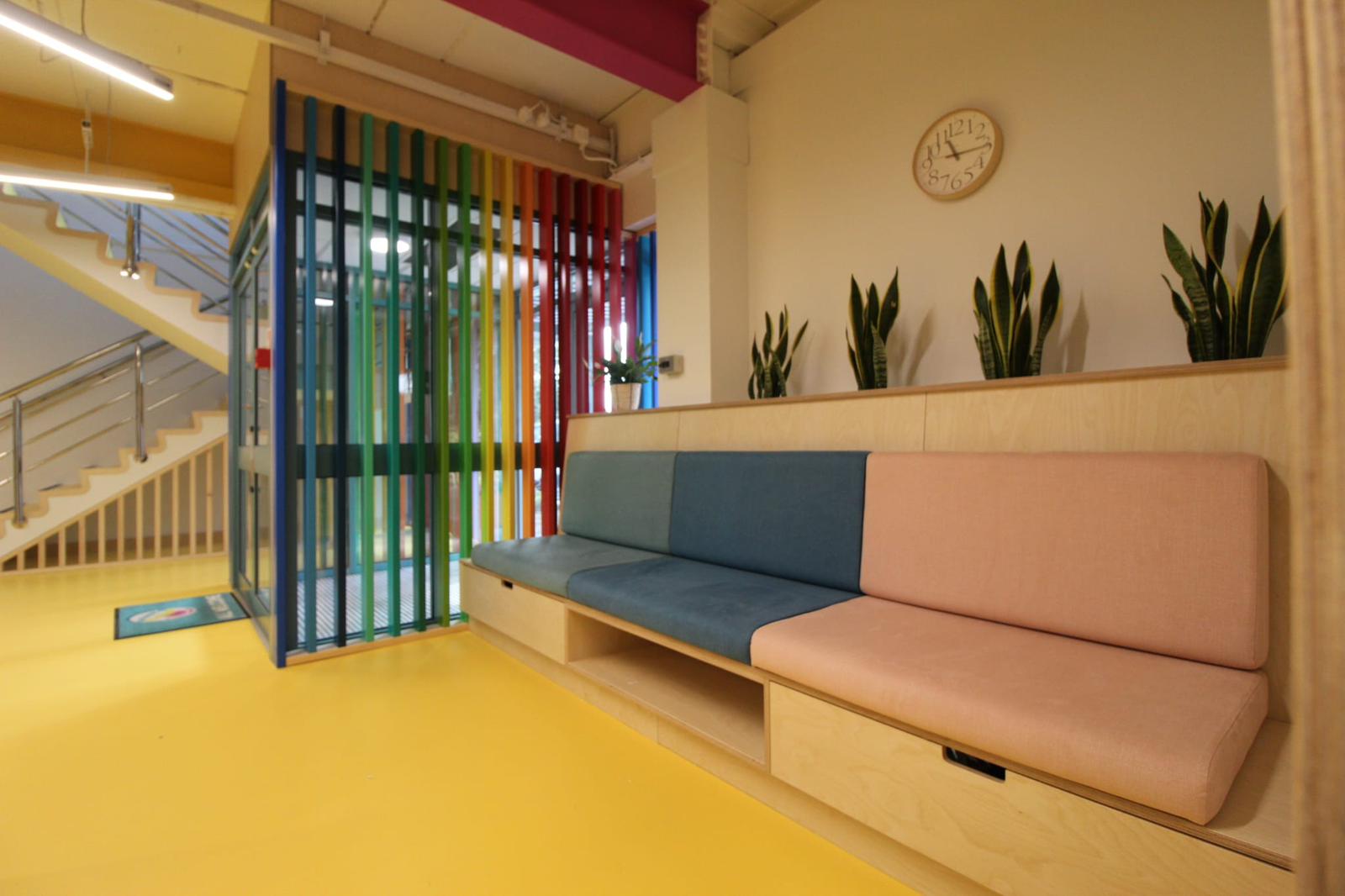 Built-in birch ply bench with pink and teal cushions and under-seat storage, in a brightly coloured school breakout area.