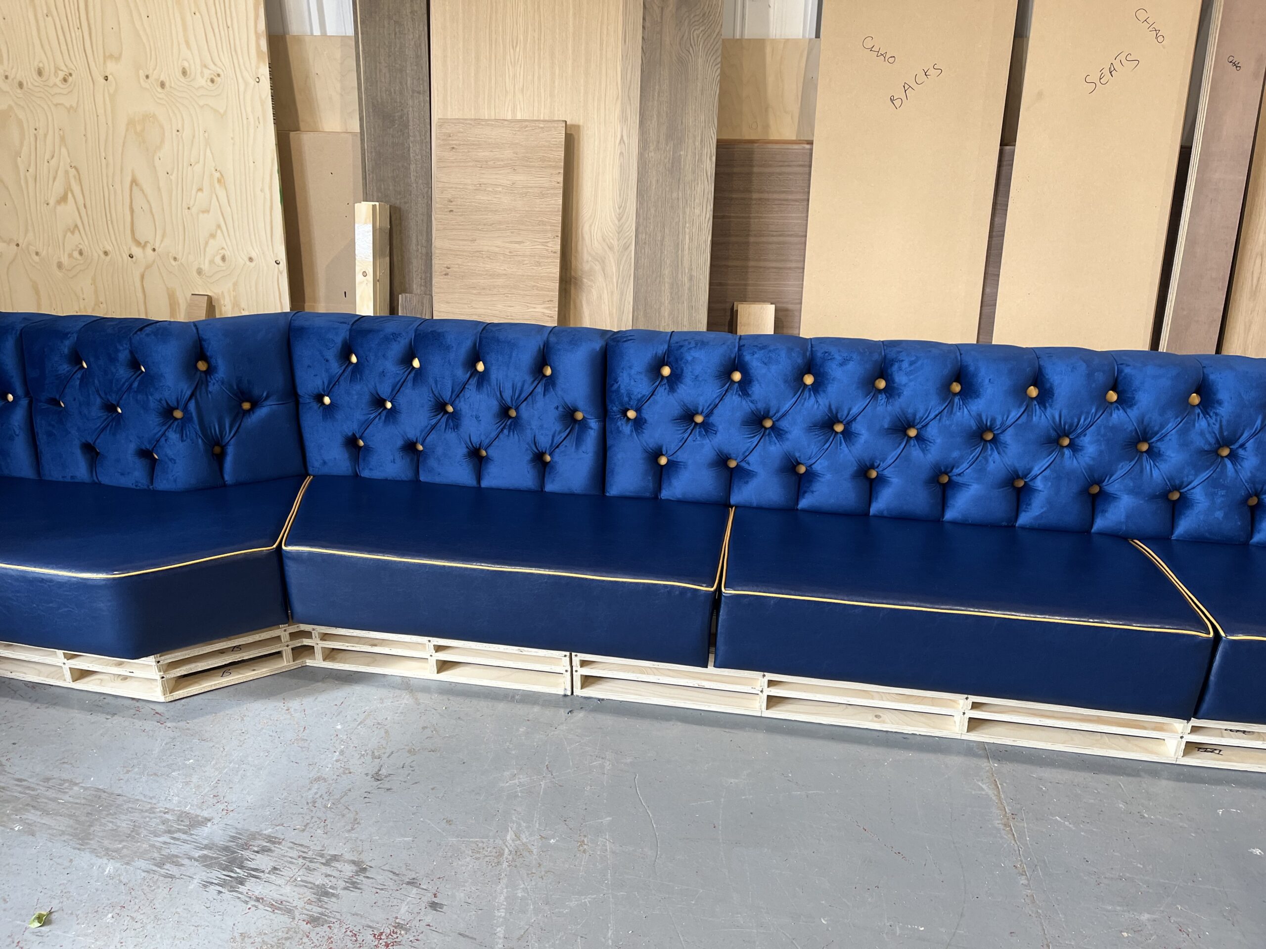 Royal blue velvet banquette with gold buttons and piping over a navy leather seat, photographed mid-build in our workshop.