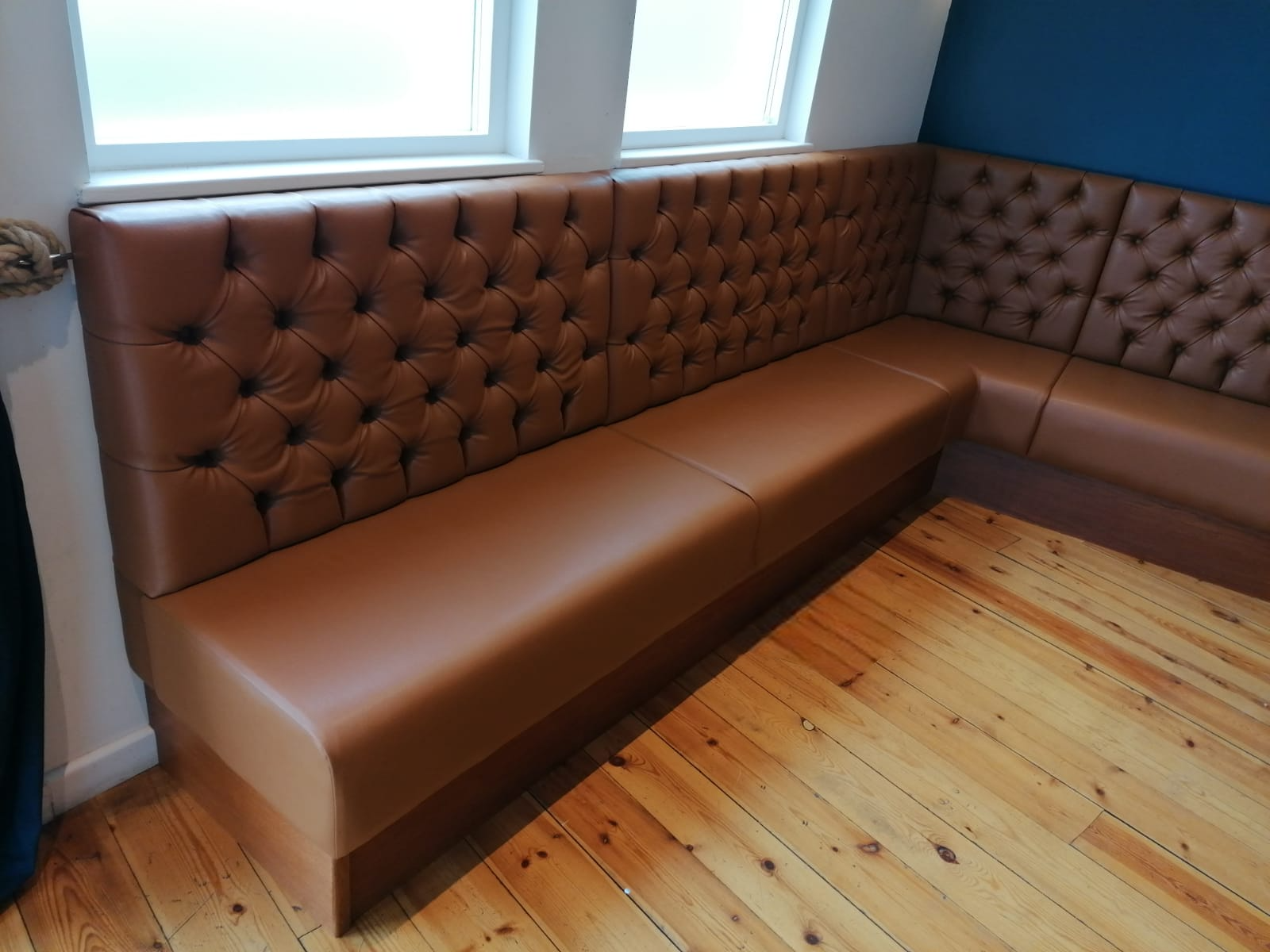 L-shaped banquette in tan leather with a deep-buttoned back, built under the windows of a loft meeting room.