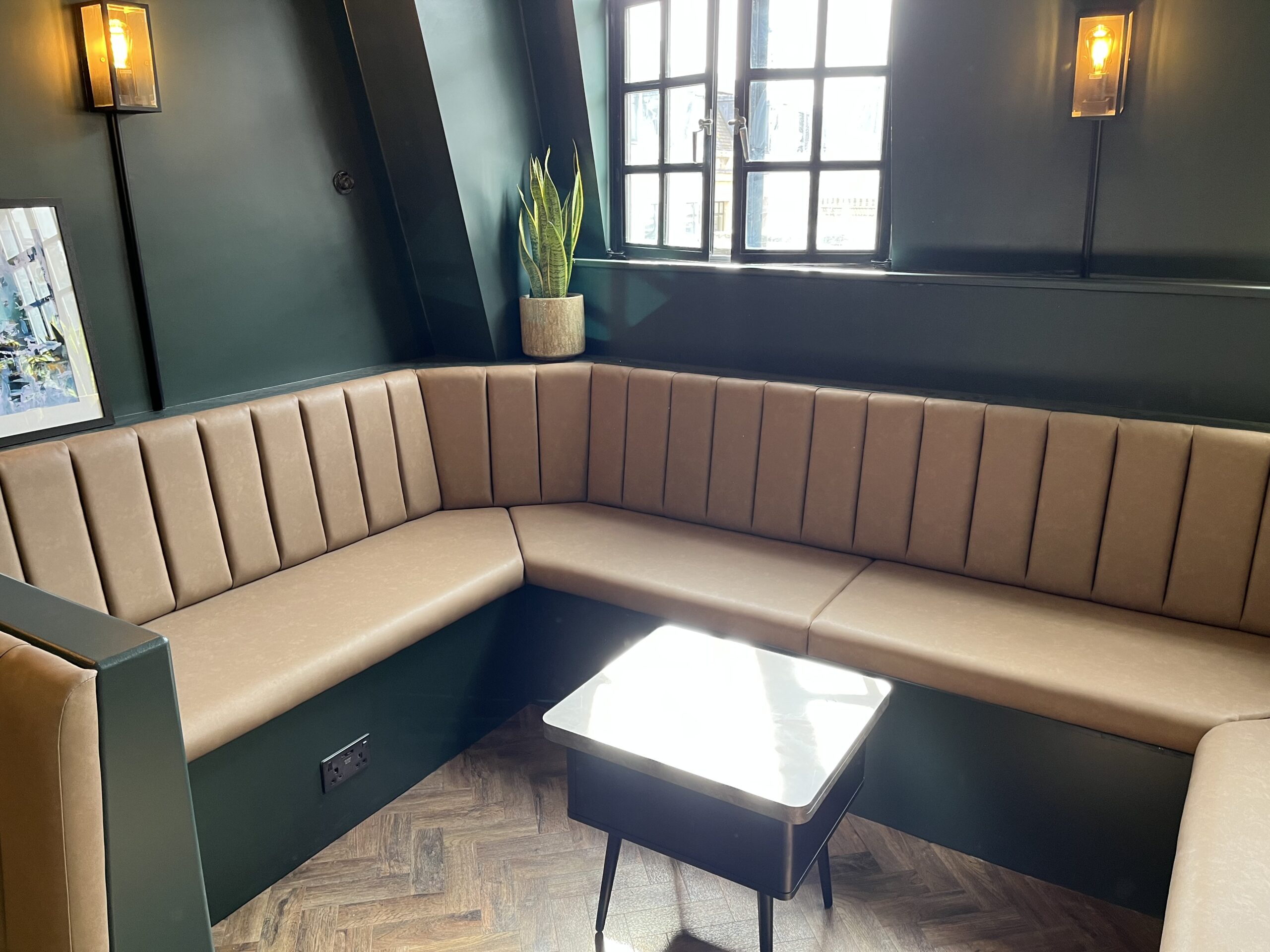 L-shaped fluted banquette in soft tan leather, set against dark green panelling and herringbone flooring.