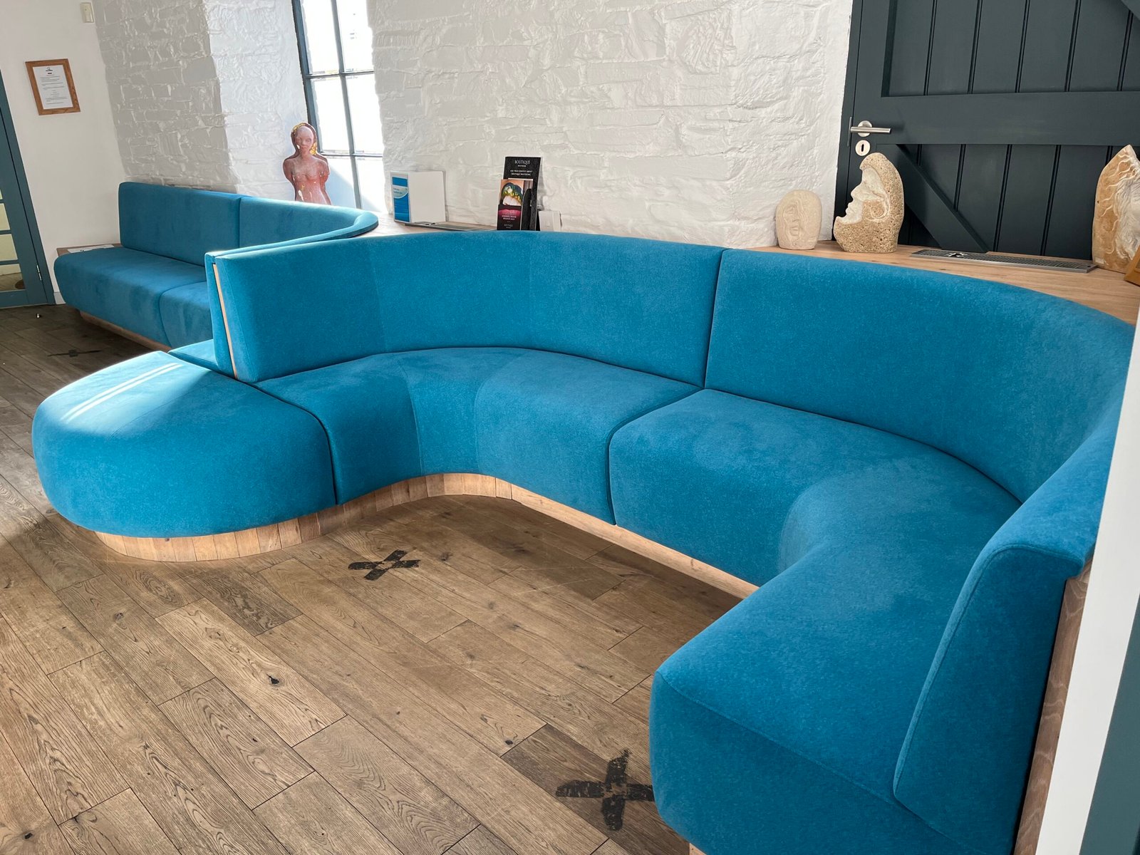 Sweeping curved bench in teal fabric on an oak plinth, shaped to follow the wall of a dental practice waiting room.