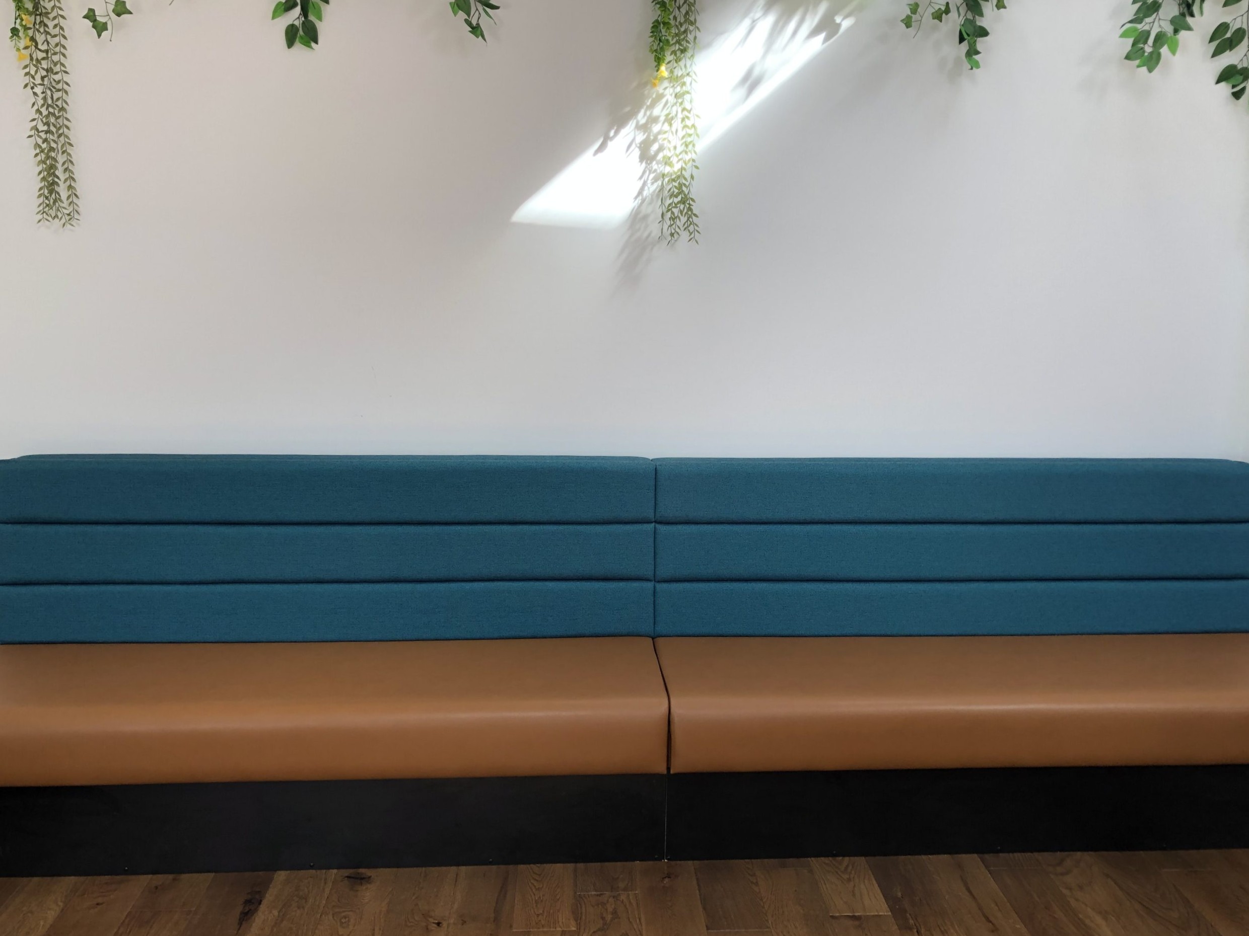 Clean-lined cafe bench pairing a tan leather seat with horizontally panelled teal fabric backrests on a dark plinth.