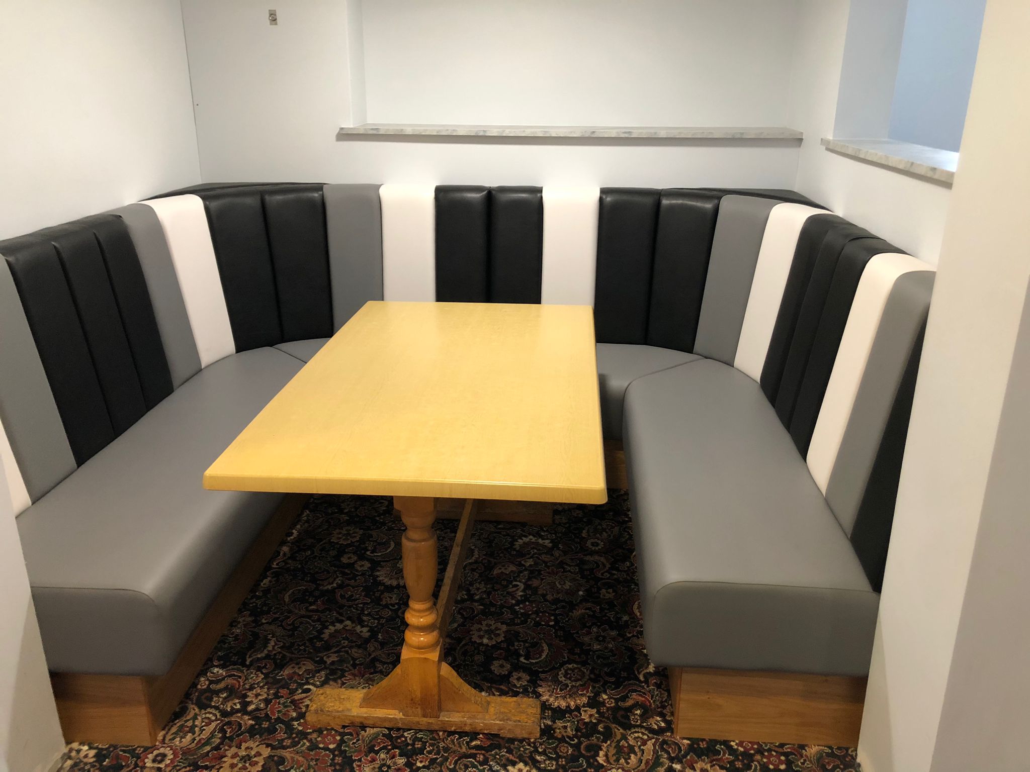 U-shaped booth with alternating black, white and grey fluted back panels above grey leather seats.