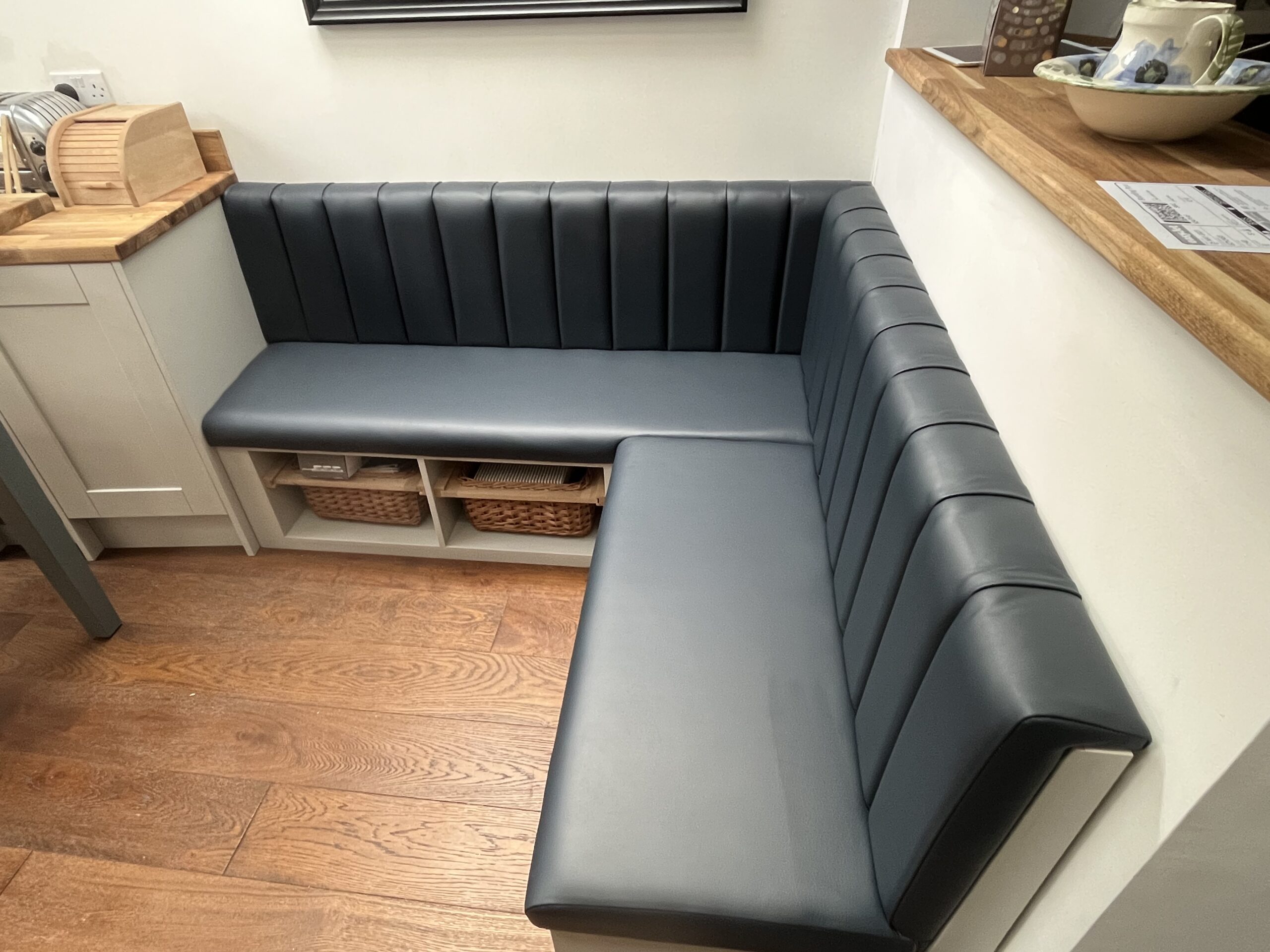 L-shaped kitchen bench in charcoal faux leather with fluted backrests and open basket storage beneath the seat.