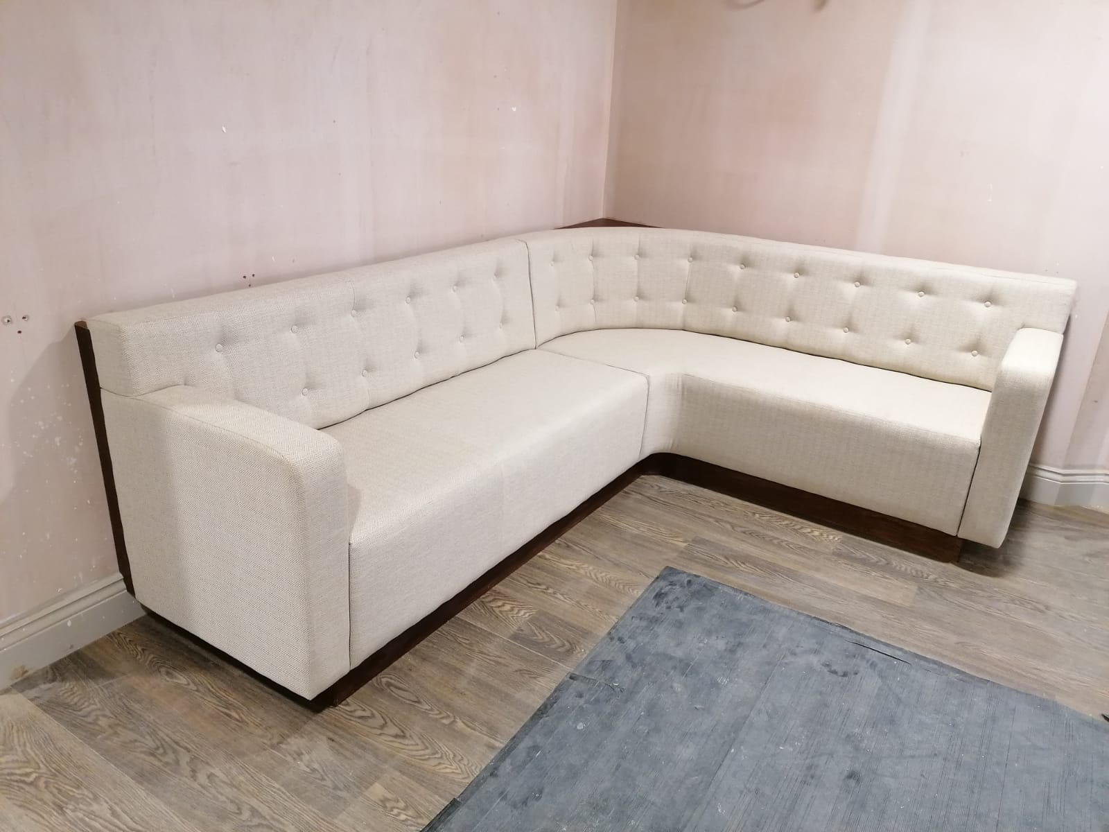 L-shaped banquette in cream herringbone tweed with a buttoned back and dark timber plinth, photographed before the fit-out completed.