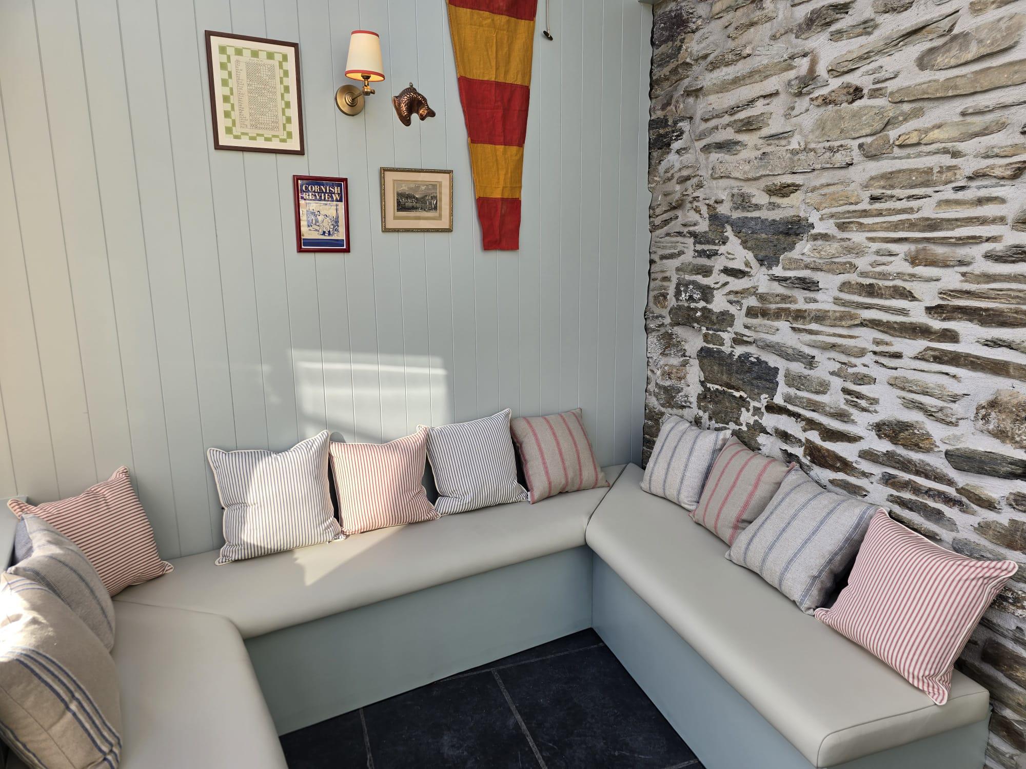 L-shaped bench in cream faux leather built into a painted garden room, dressed with striped ticking cushions.
