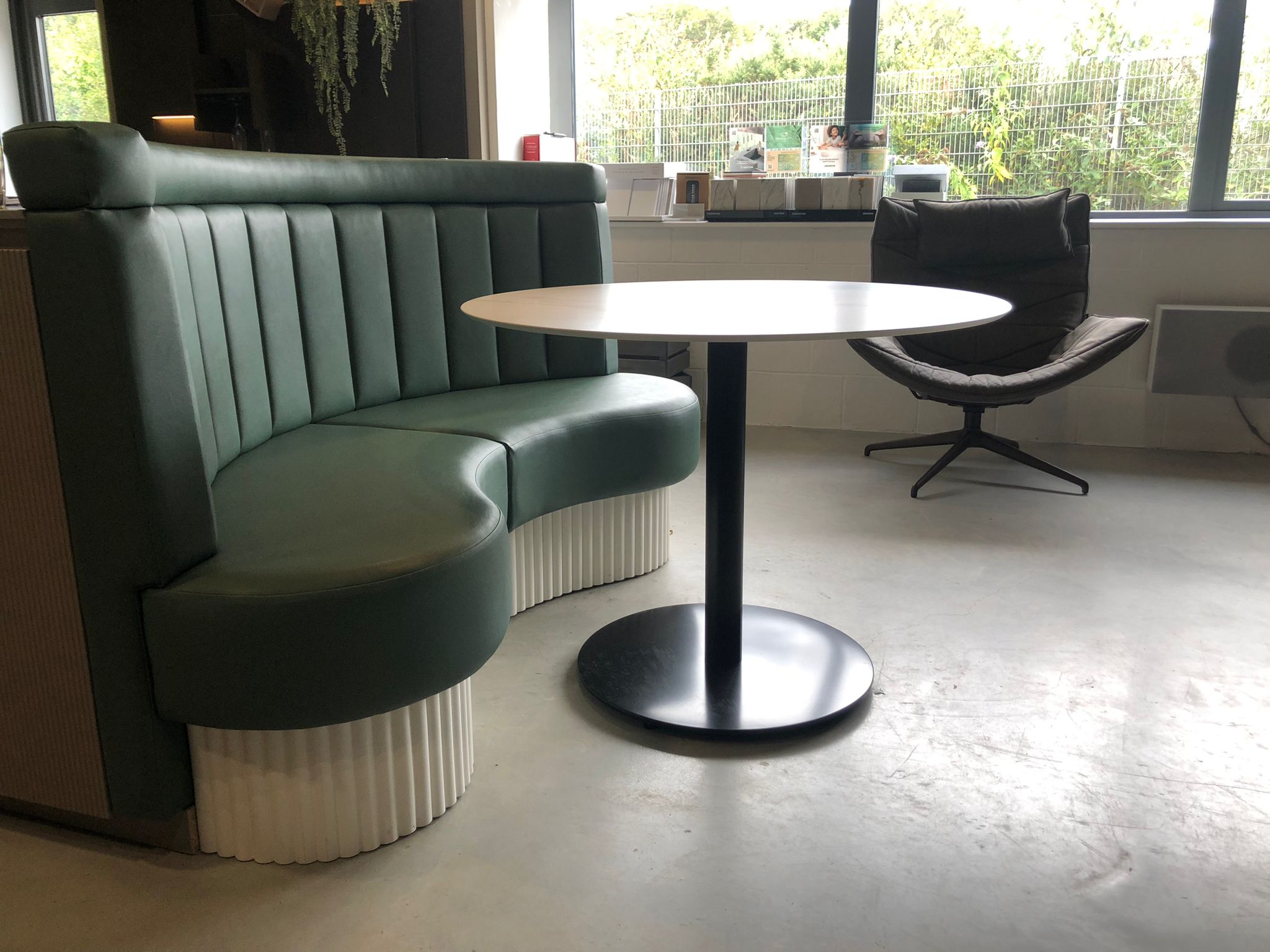 Curved booth in sage green leather with a fluted back and white ribbed plinth, built for a showroom meeting area.