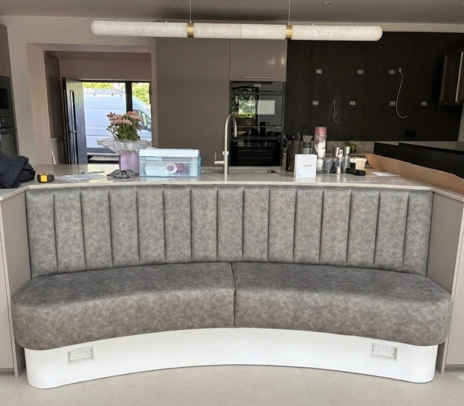 Curved fluted banquette in mottled grey leather wrapped around a kitchen island on a white painted plinth.