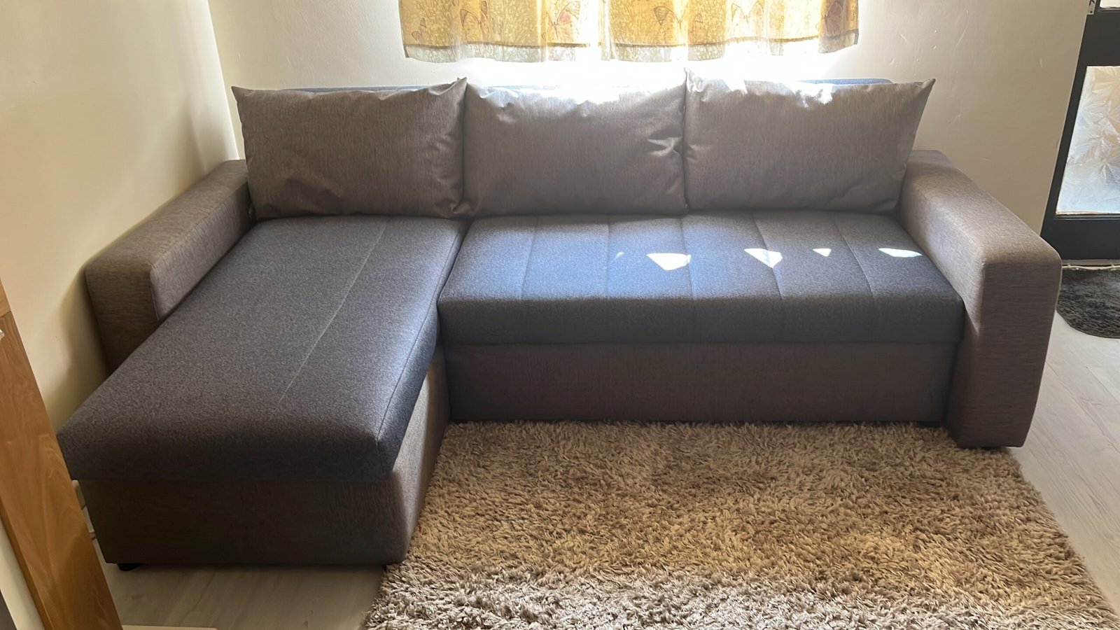Deep grey corner sofa with a chaise end and loose back cushions, made for a compact living room.