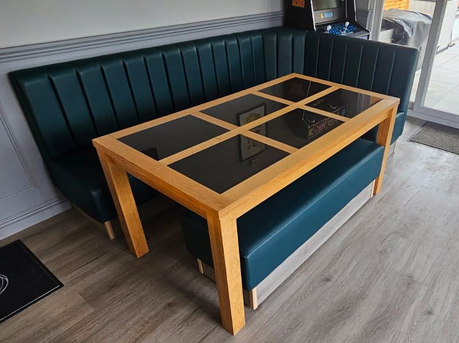 L-shaped corner bench in teal leather with a fluted back, built around an oak games table in a home bar.