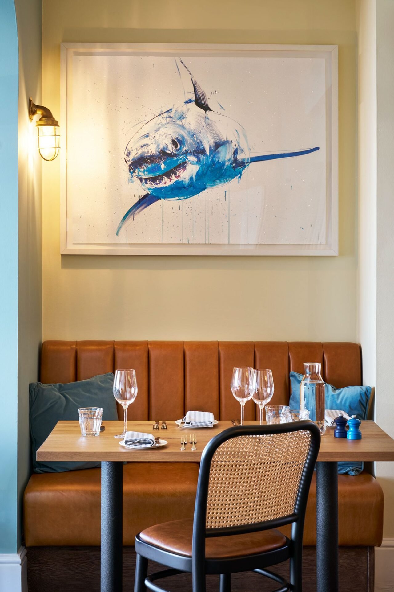 Two-seater tan leather booth with a fluted back and teal scatter cushions, set beneath a framed shark print.