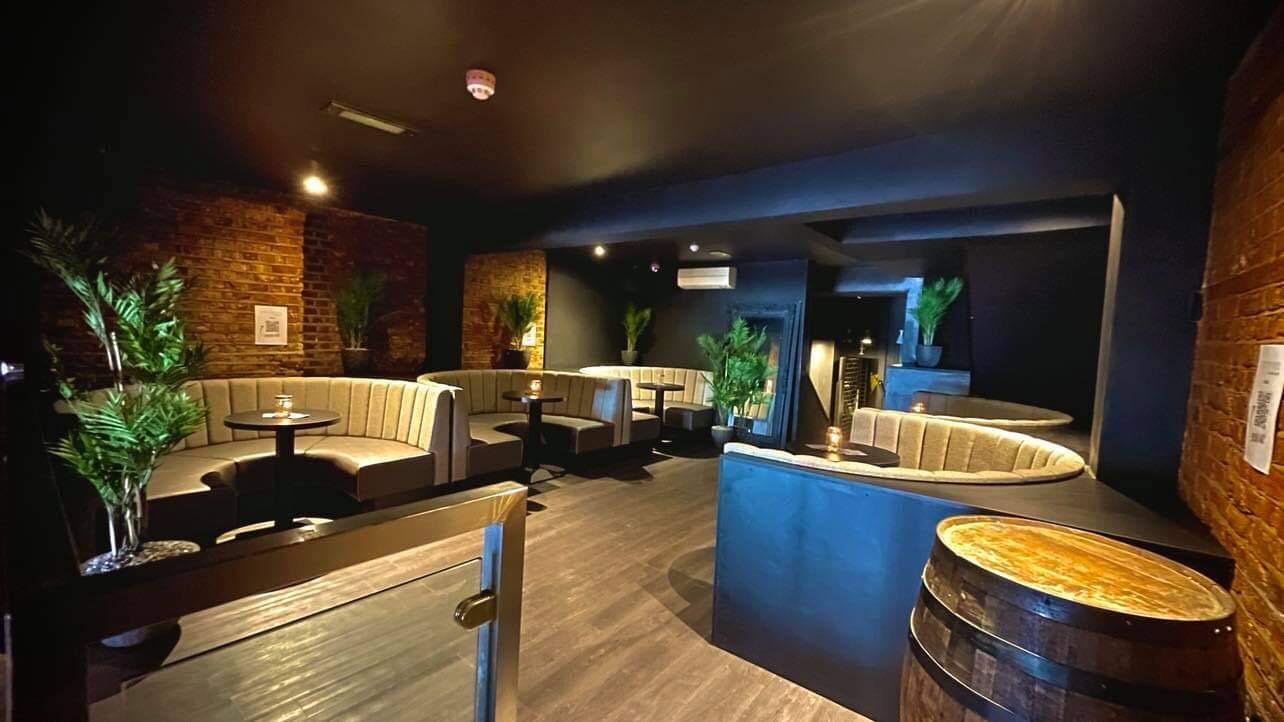Horseshoe booths in cream fluted leather set against exposed brick and dark walls in a basement cocktail bar.