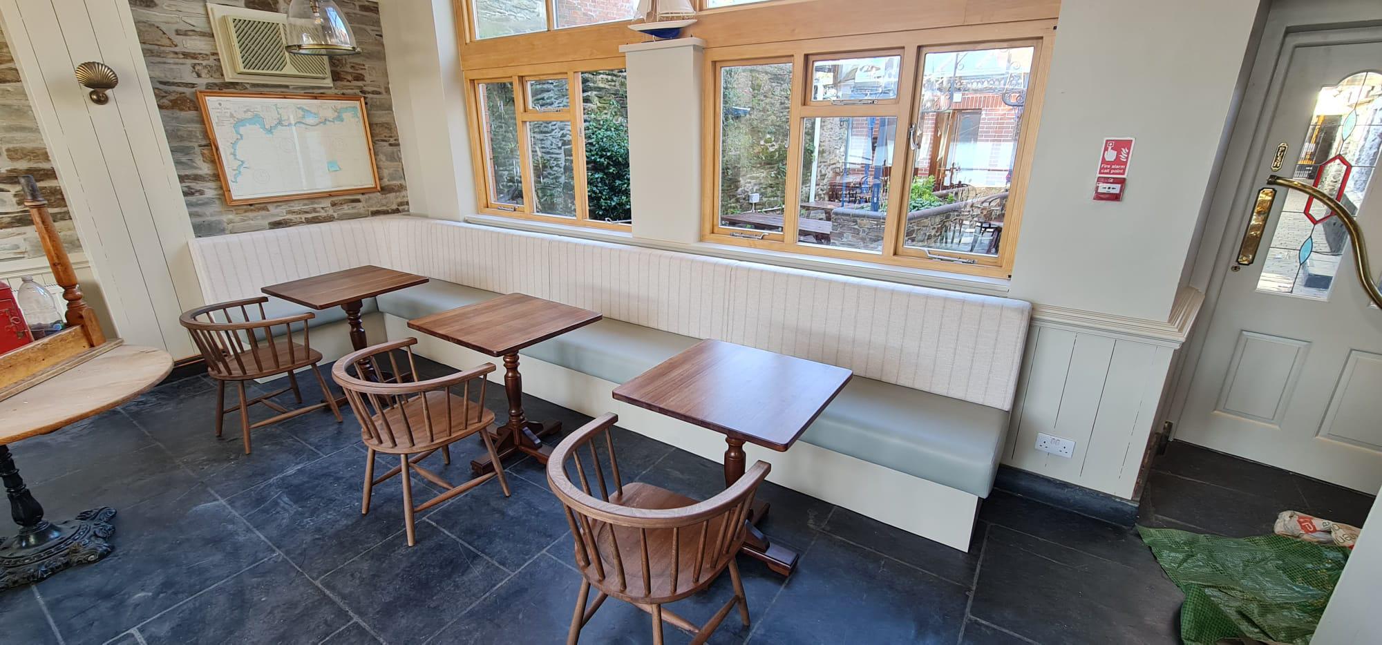 Long window bench with a sage leather seat and cream striped backrest, built along the stone wall of a harbourside pub.