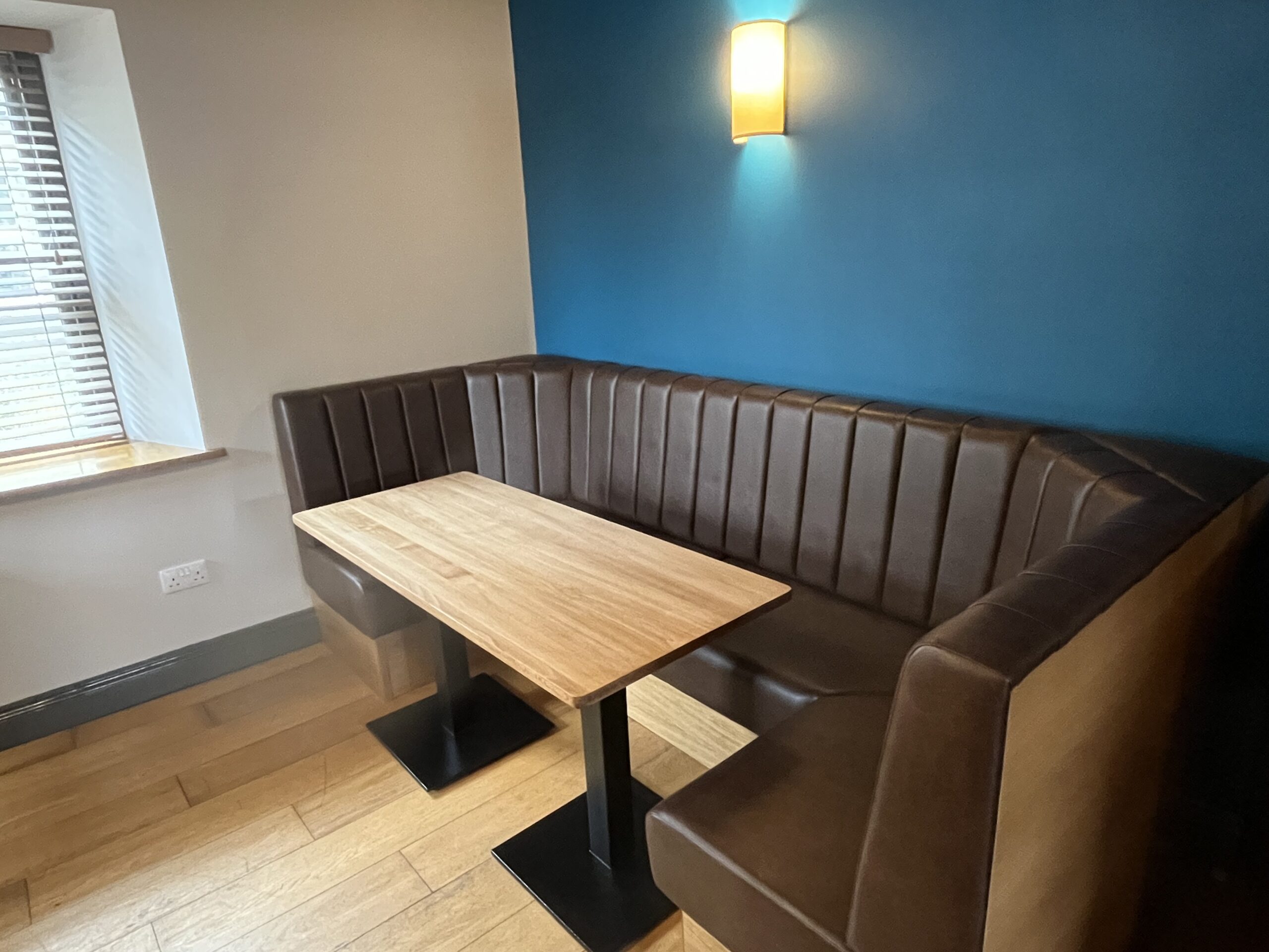 Corner booth in dark brown faux leather with fluted backrests, paired with solid oak tables on cast iron bases.