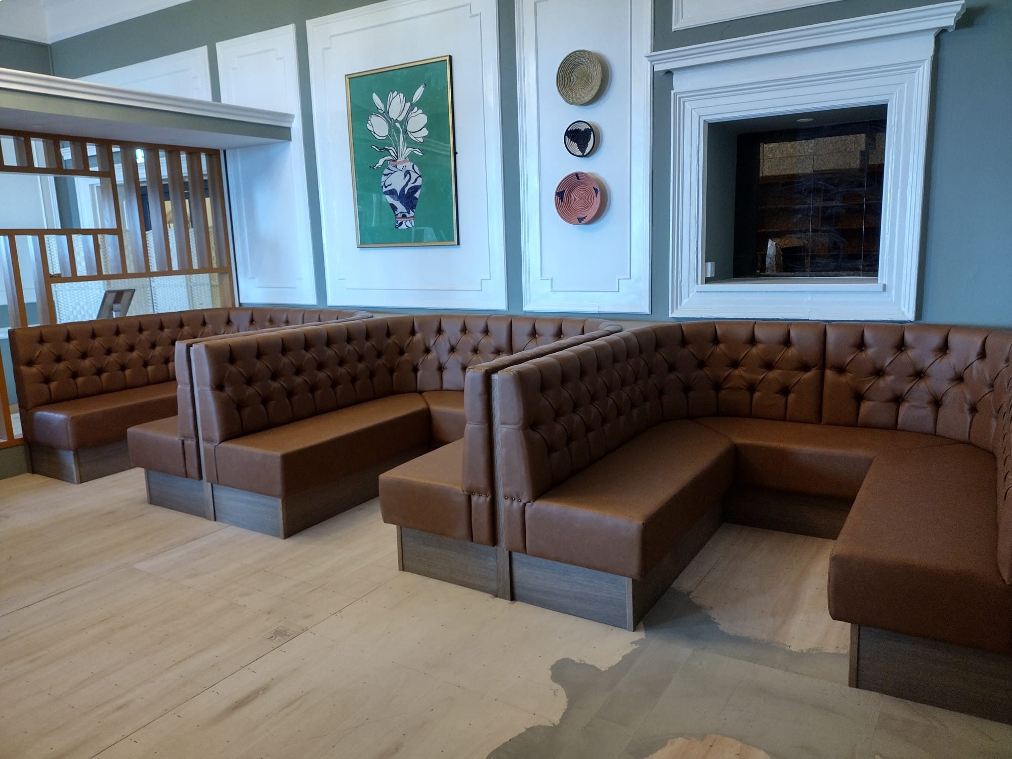Back-to-back booths in tan leather with classic deep-buttoned backs on oak plinths, laid out for a hotel dining room.
