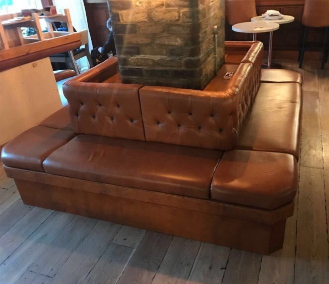 Free-standing double-sided booth in tan leather with buttoned backs, built around a brick pillar in a bar.