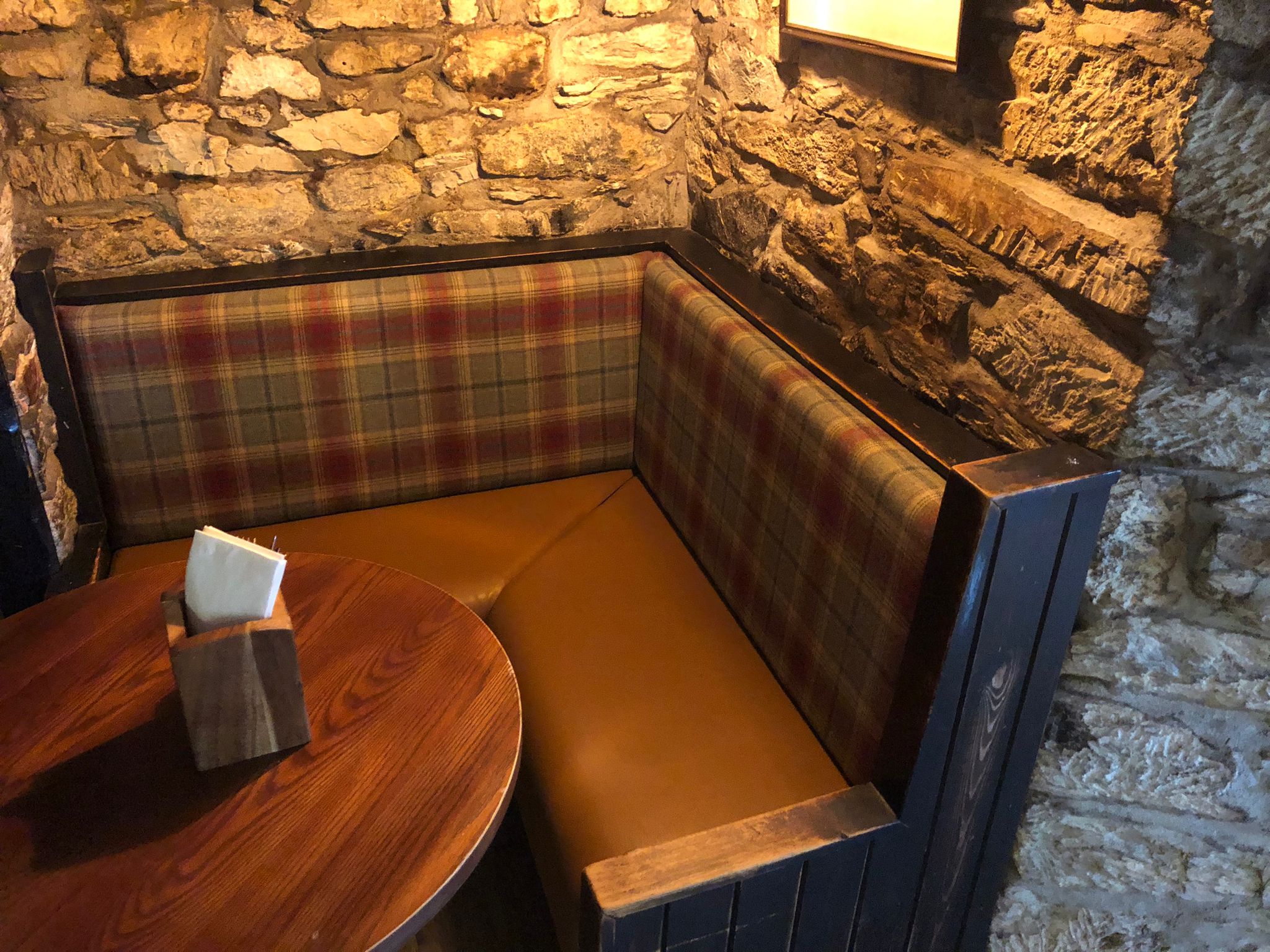 Corner settle with a tartan wool back and tan leather seat, set into the stone wall of a country pub.