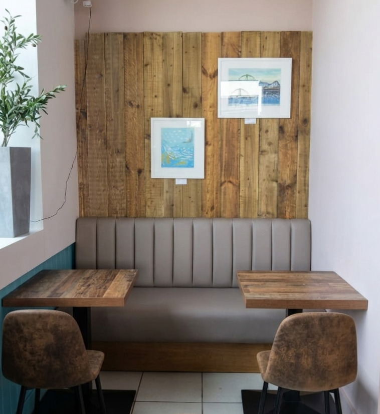 Taupe fluted banquette set against a reclaimed timber feature panel, with two rustic tables and tub chairs.