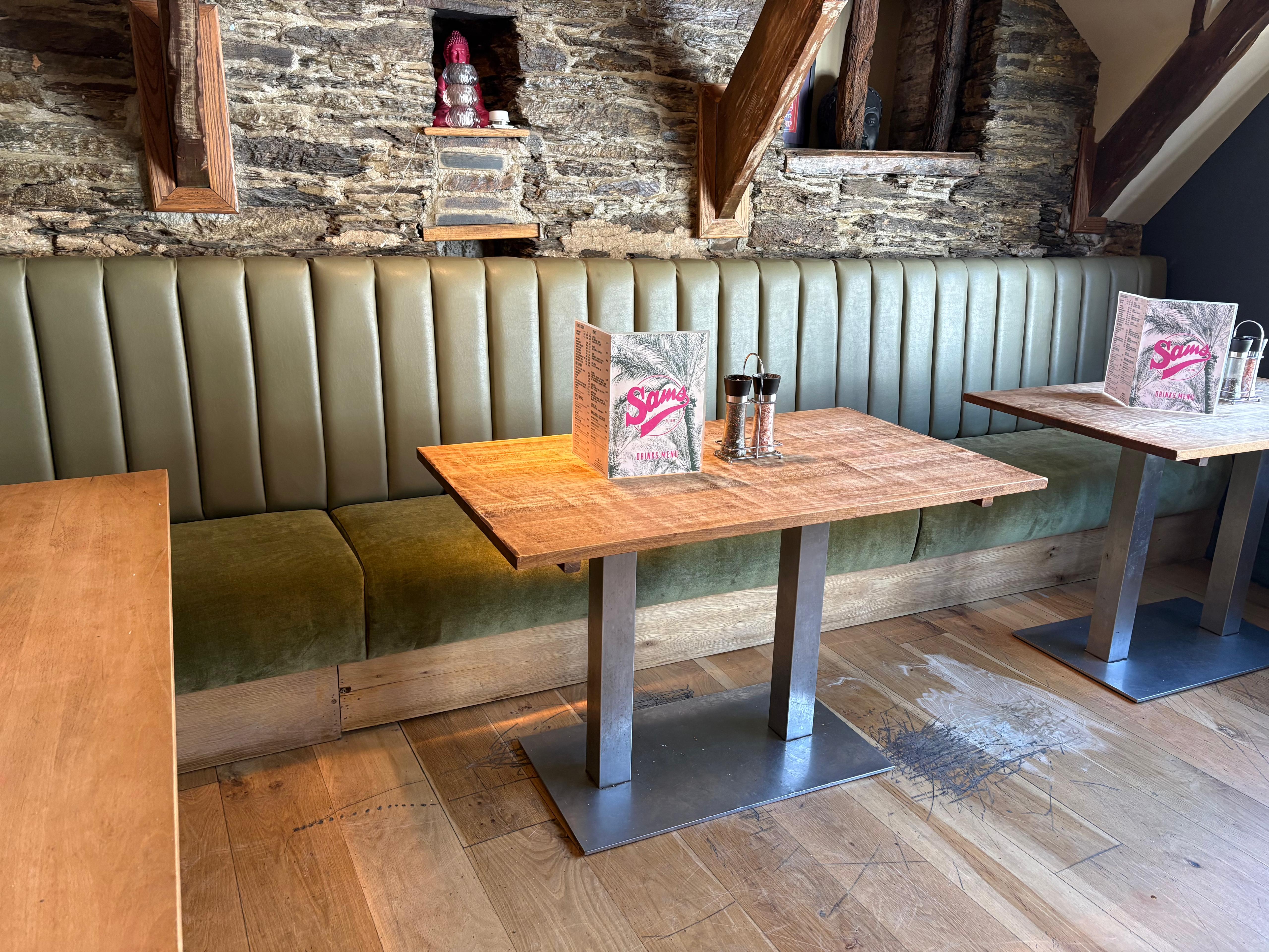 U-shaped banquette in taupe suede wrapping a snug corner of a cocktail bar, lit by a woven pendant.