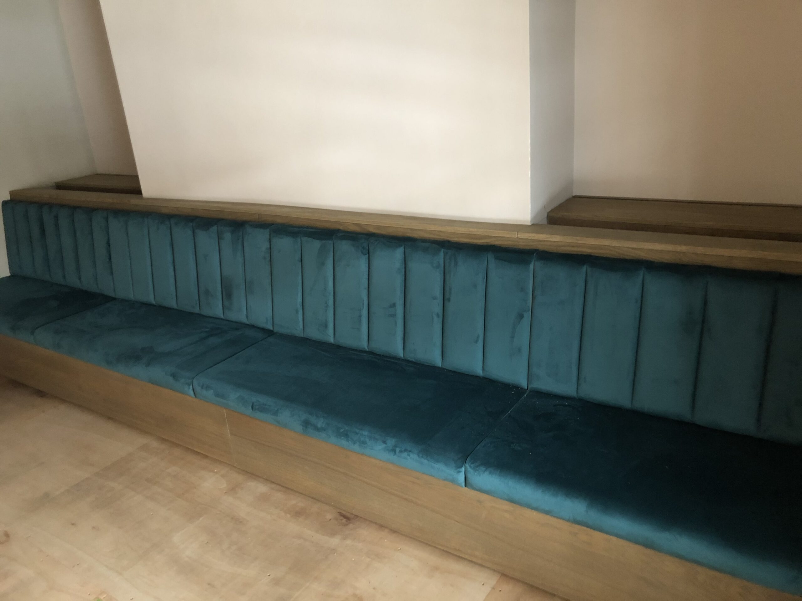 Low fluted bench in teal velvet built into an oak plinth and capping shelf for a contemporary dining room.
