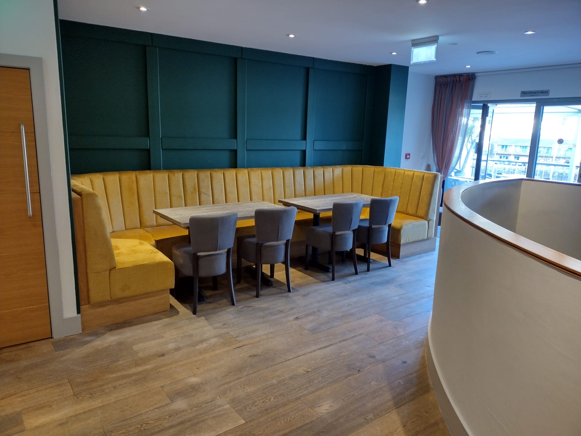 High-backed fluted banquette in ochre velvet wrapping a corner of a teal-panelled restaurant.