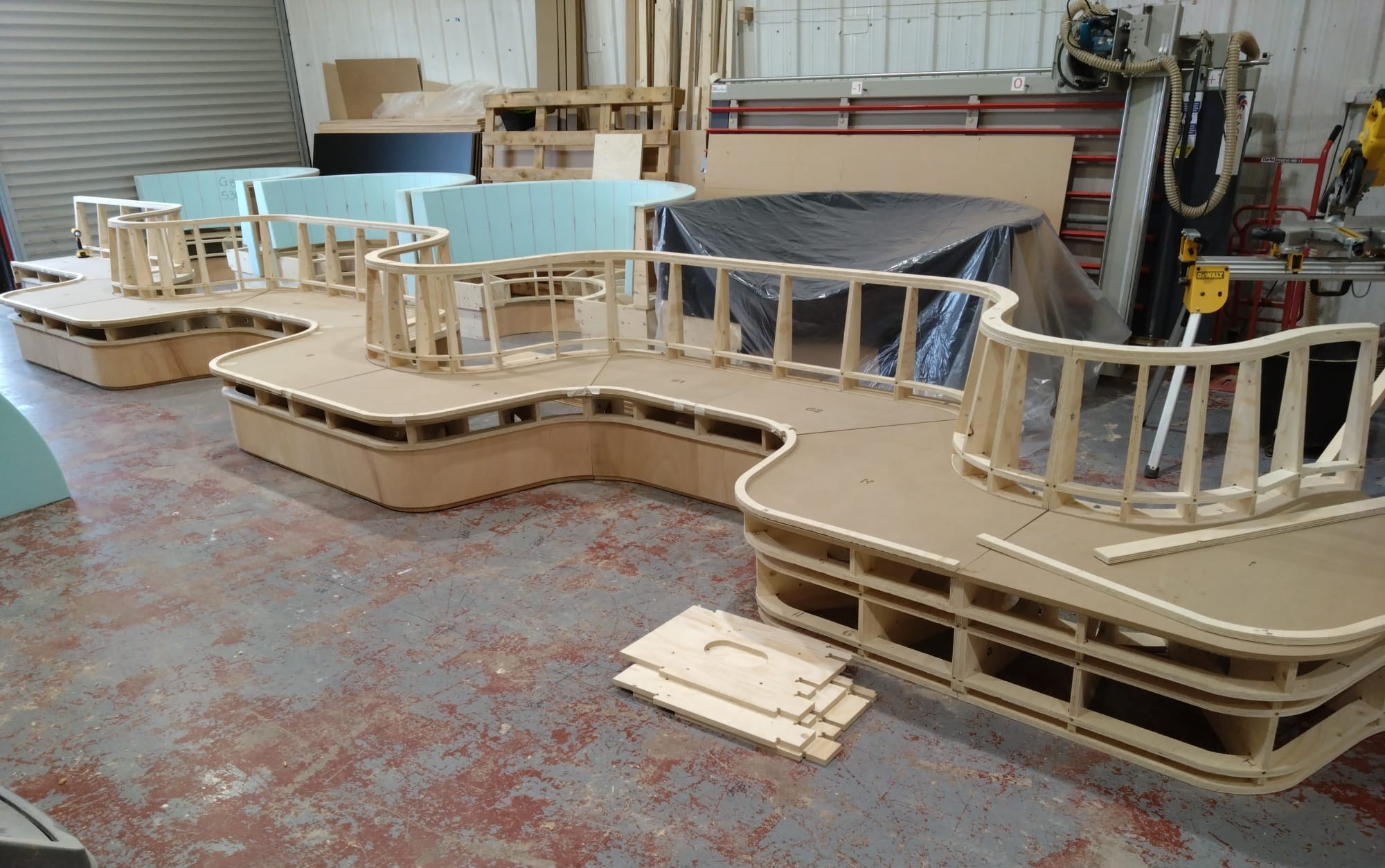 raw wooden timber frames of bespoke curved serpentine banquette seating under construction inside the Unique Seating workshop